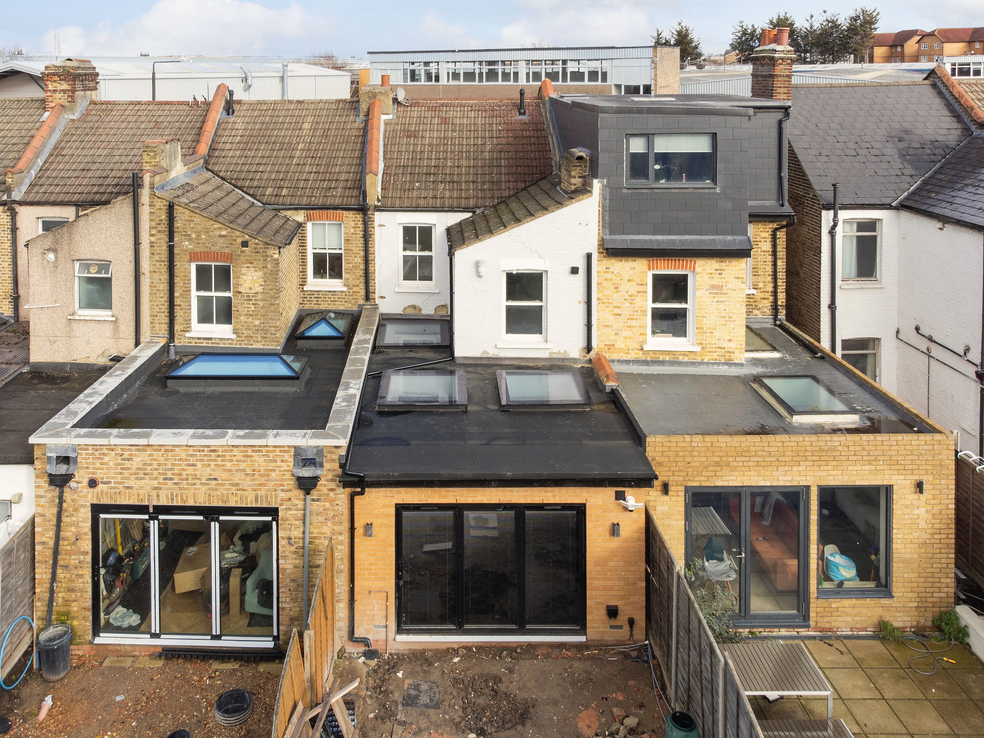 Drone view of the rear extension with its black flat roof and rooflights, between two neighbouring houses