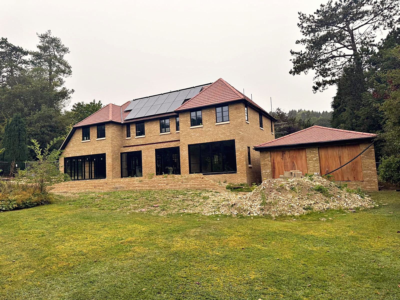 A new brick house with a clay tile roof, solar panels and black steel-framed windows, nearing completion