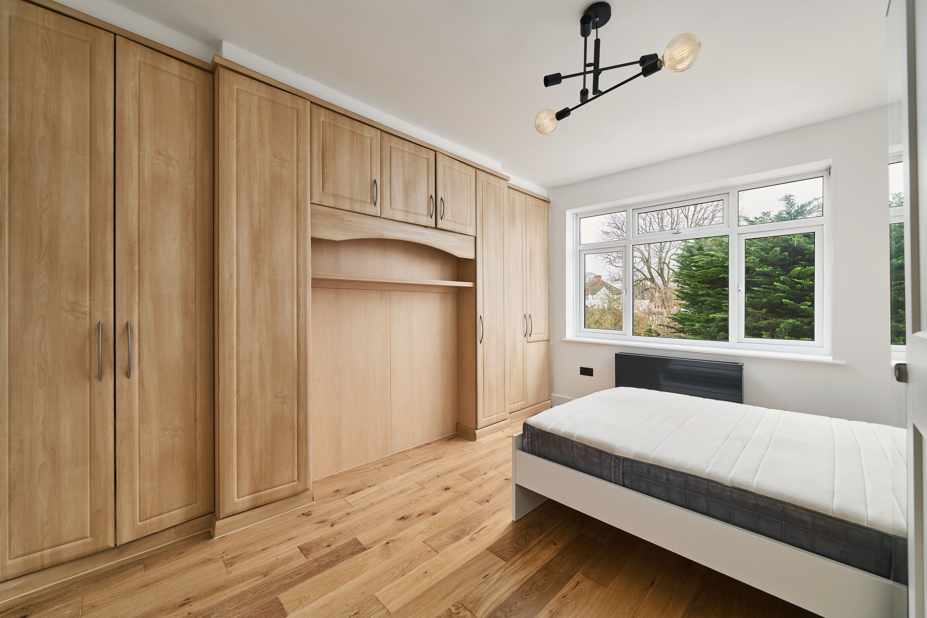 A bedroom with fitted oak-effect wardrobes and an overhead cupboard built around the bed