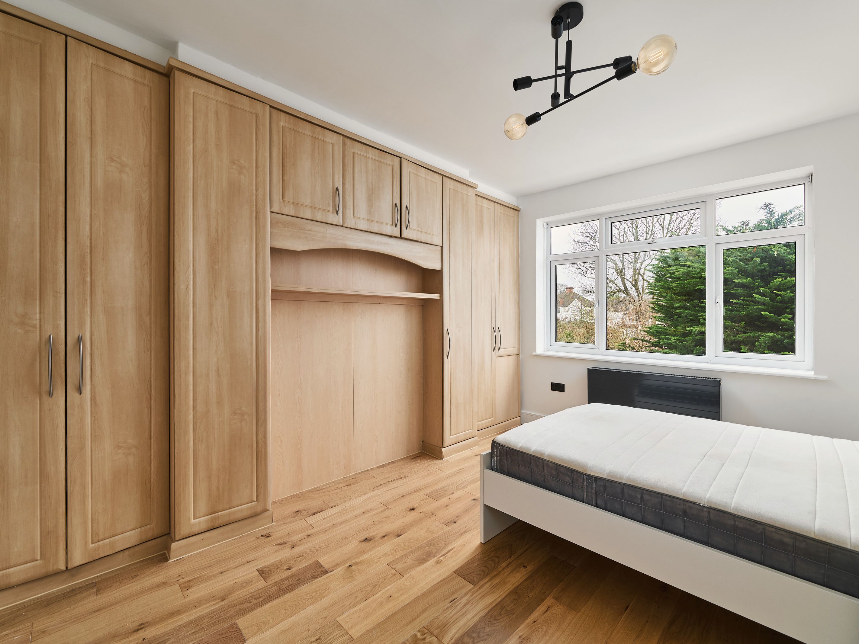 A bedroom with fitted oak-effect wardrobes and an overhead cupboard built around the bed