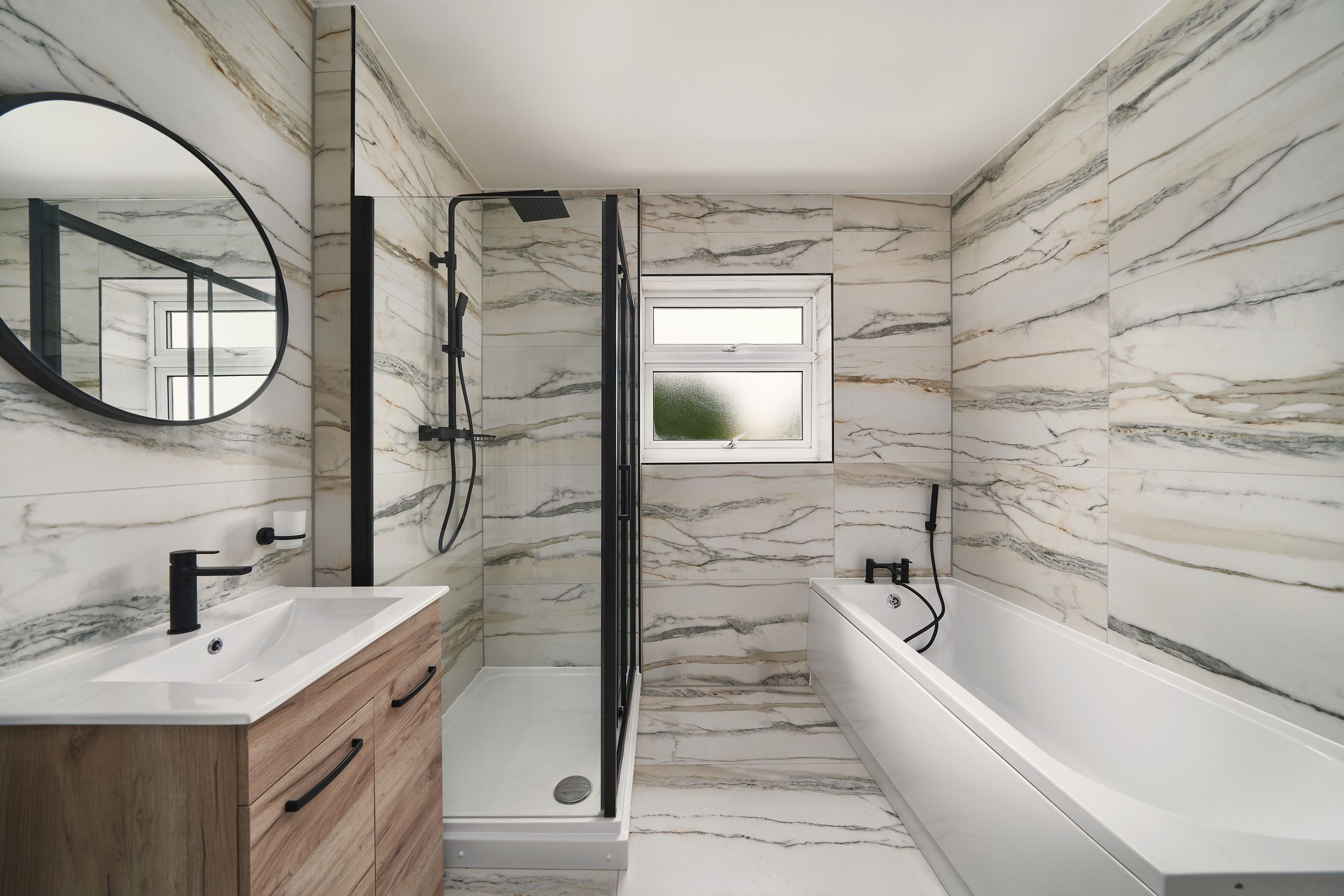 A refurbished bathroom with marble-effect tiles, a bath, a black-framed shower and a wood-effect vanity unit