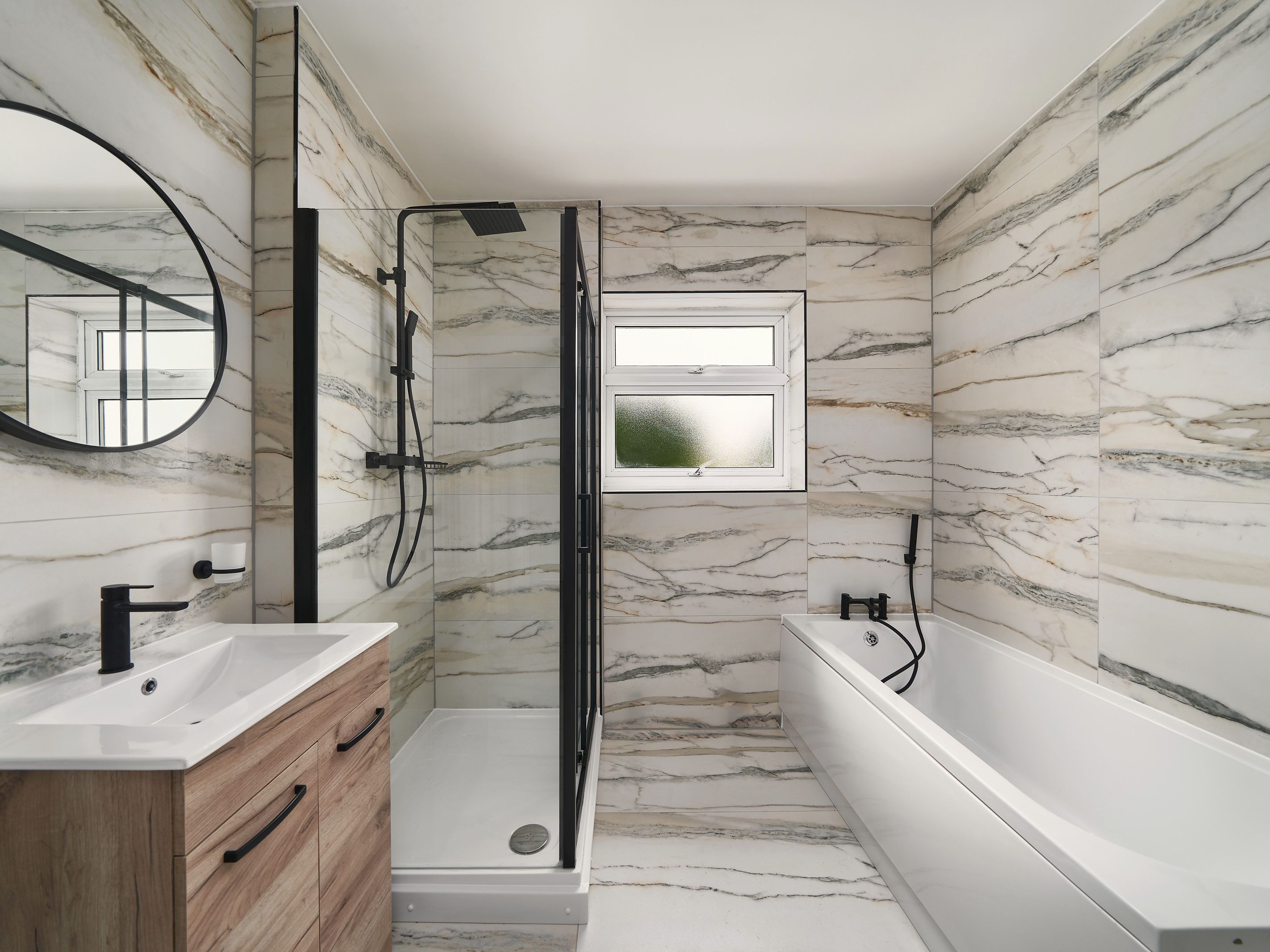 A refurbished bathroom with marble-effect tiles, a bath, a black-framed shower and a wood-effect vanity unit