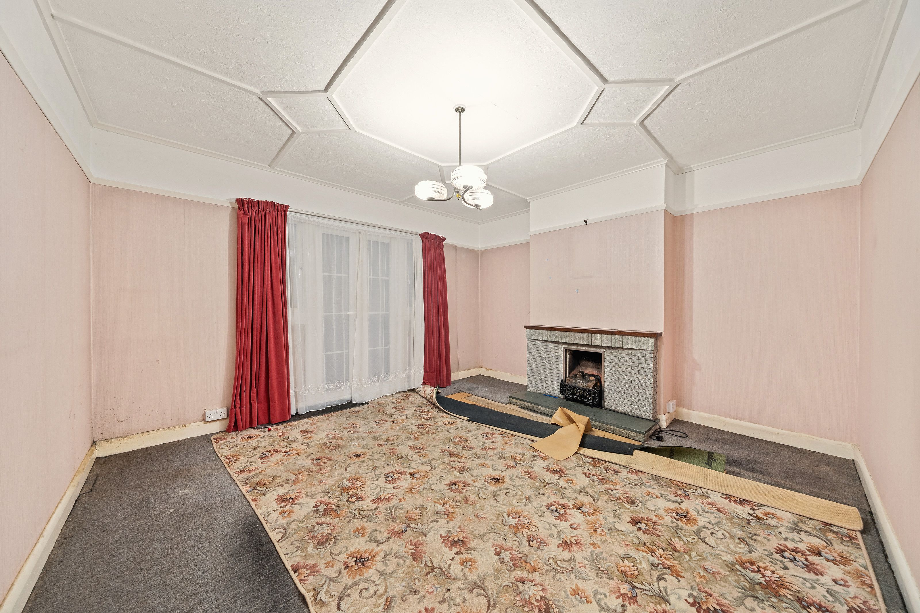 A room before the work, with pink walls, a fireplace and red curtains