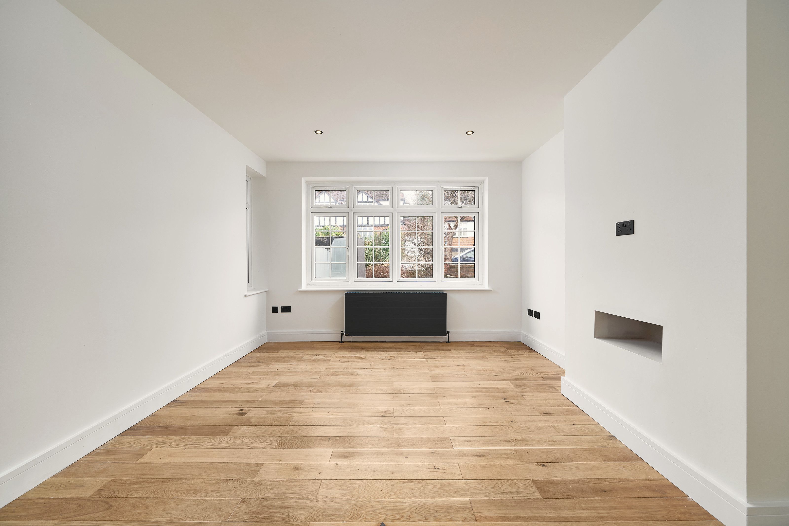 The front room looking towards the window, with downlights and a recess in the chimney breast