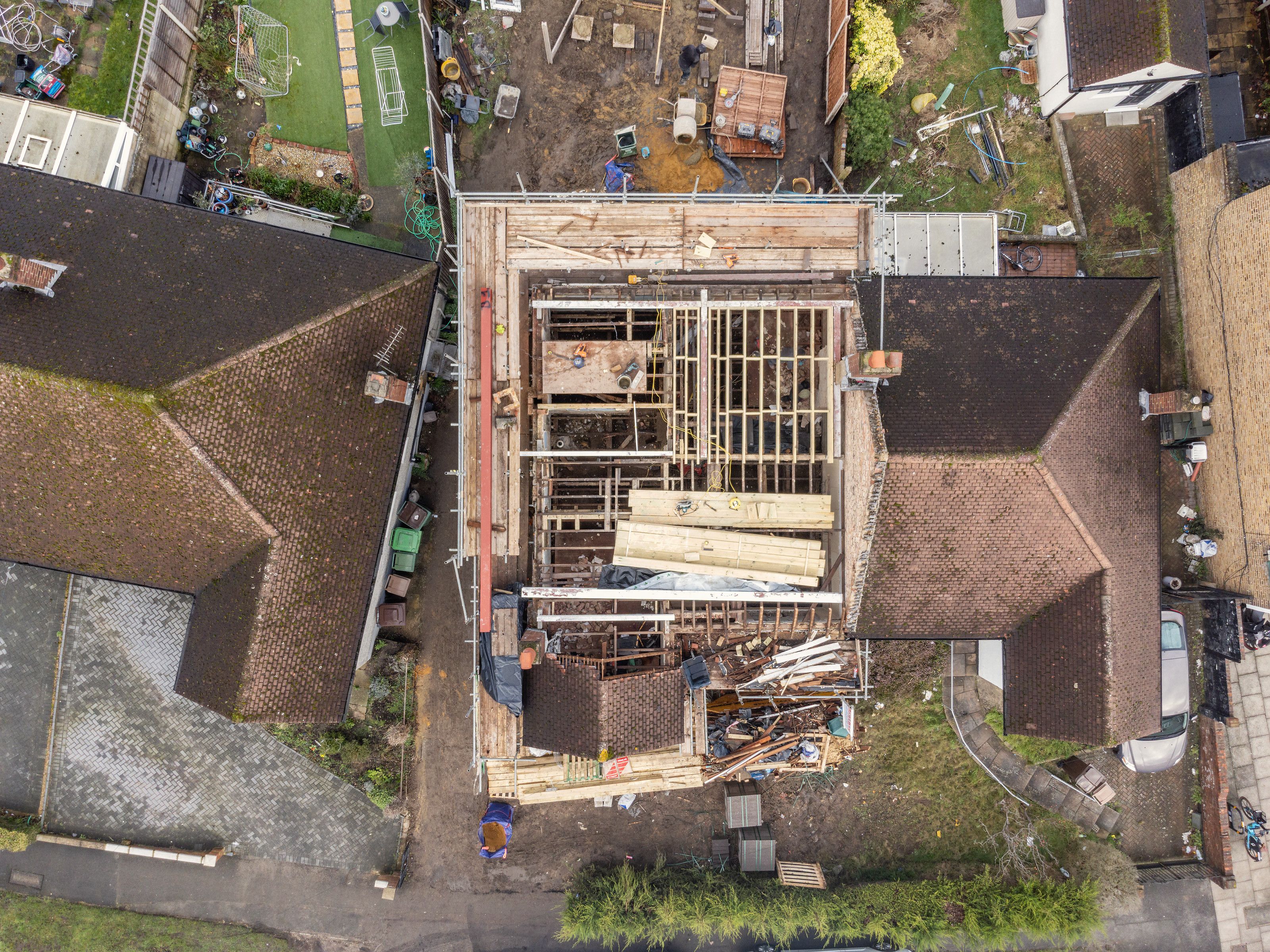 Drone view looking straight down on the bungalow with its roof off and new timber framing inside