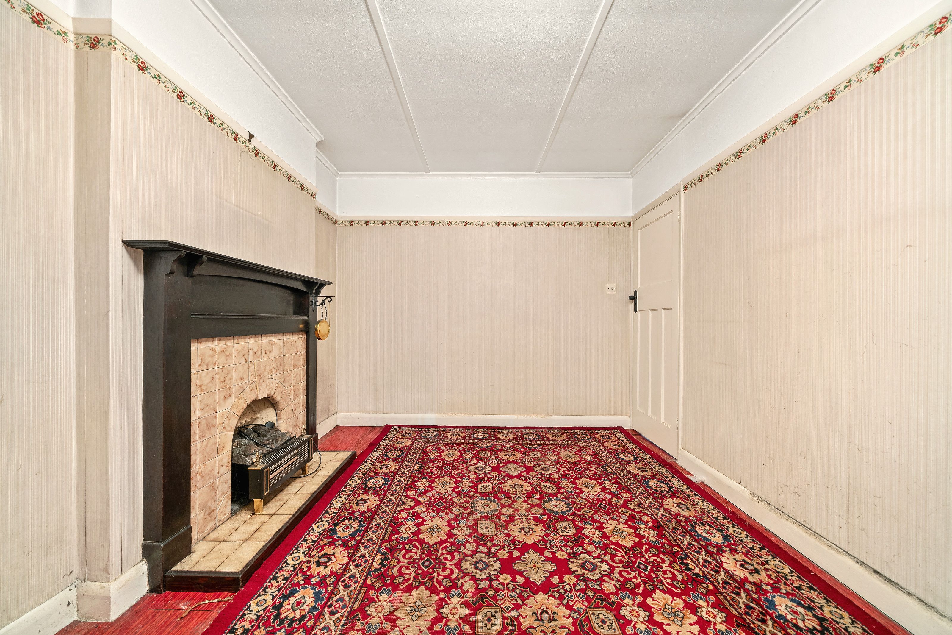 A front room before the work, with a tiled fireplace and a red patterned rug