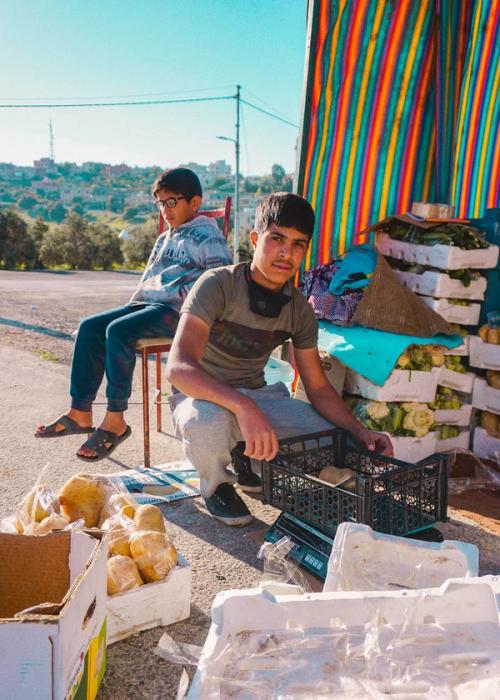 The early morning in Badr al-Jadeedah. A young boy preparing his produce for the day in his tent (Basta), while his little brother sits. Badr al-Jadeedah still ...