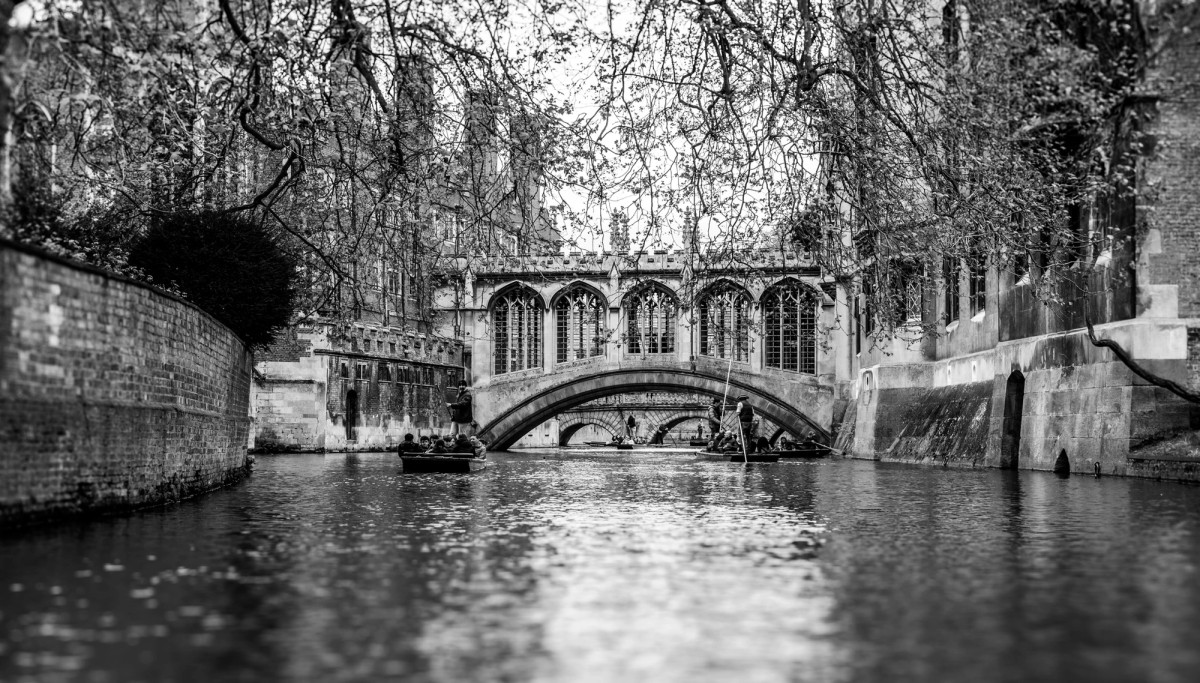 The Bridge of Sighs at St John's College, Cambridge, seen from water level in black and white, with punts passing beneath its arch.