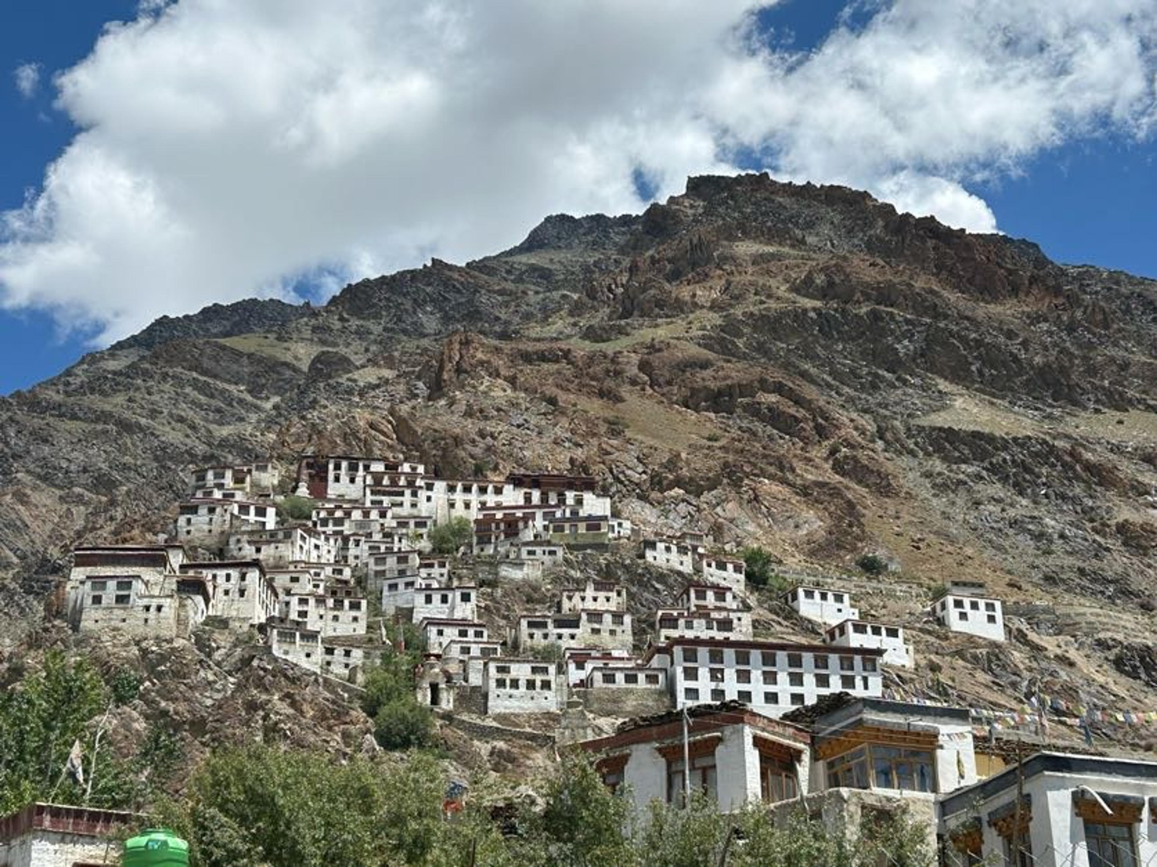 Karsha monastery's whitewashed buildings stacked down a steep rocky mountainside, under blue sky and white clouds