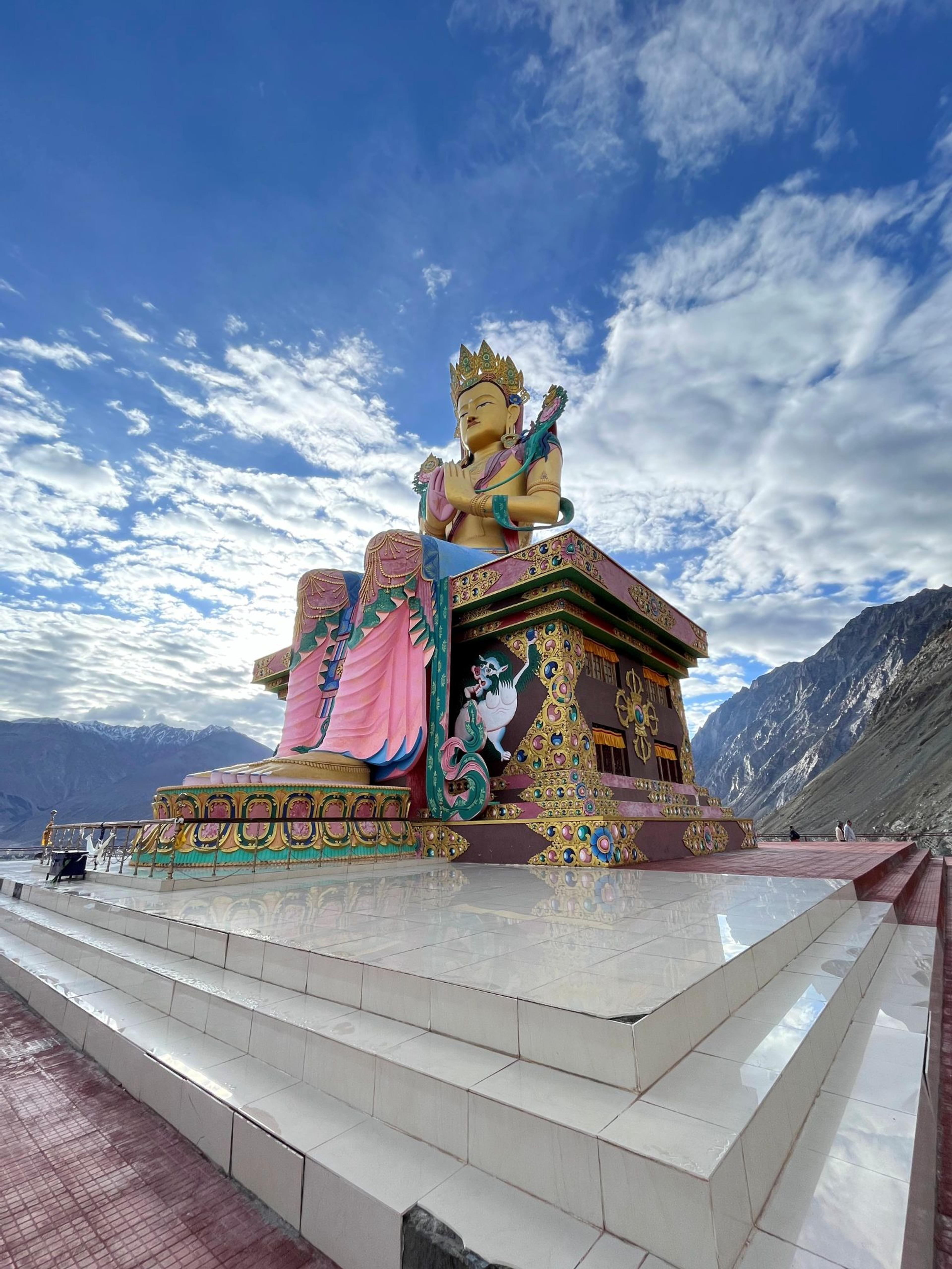 Giant golden-faced Maitreya Buddha statue at Diskit, seated on a painted plinth above the Nubra valley, under a blue sky