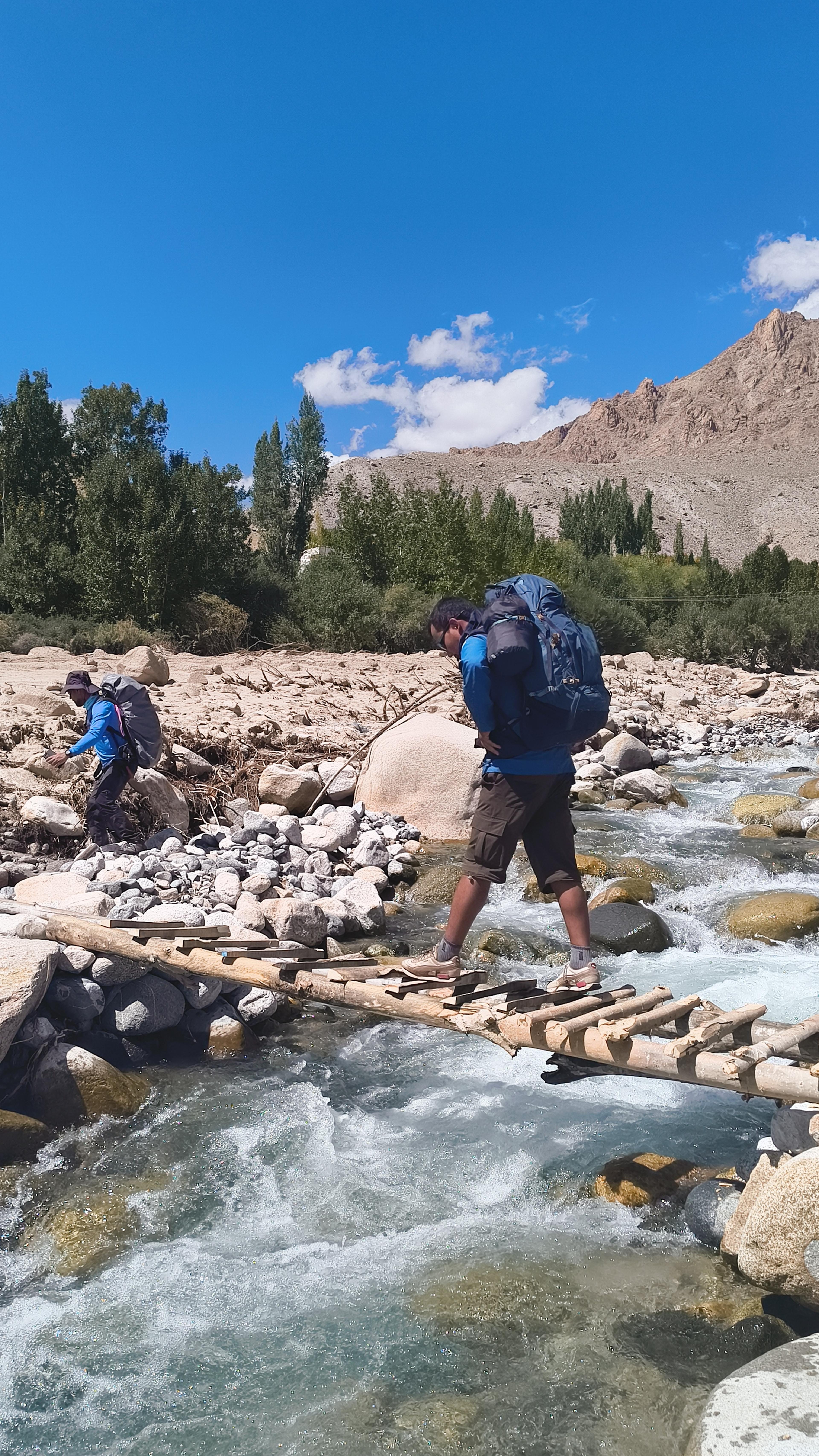 Trekker with a large backpack crossing a stream on a narrow log bridge