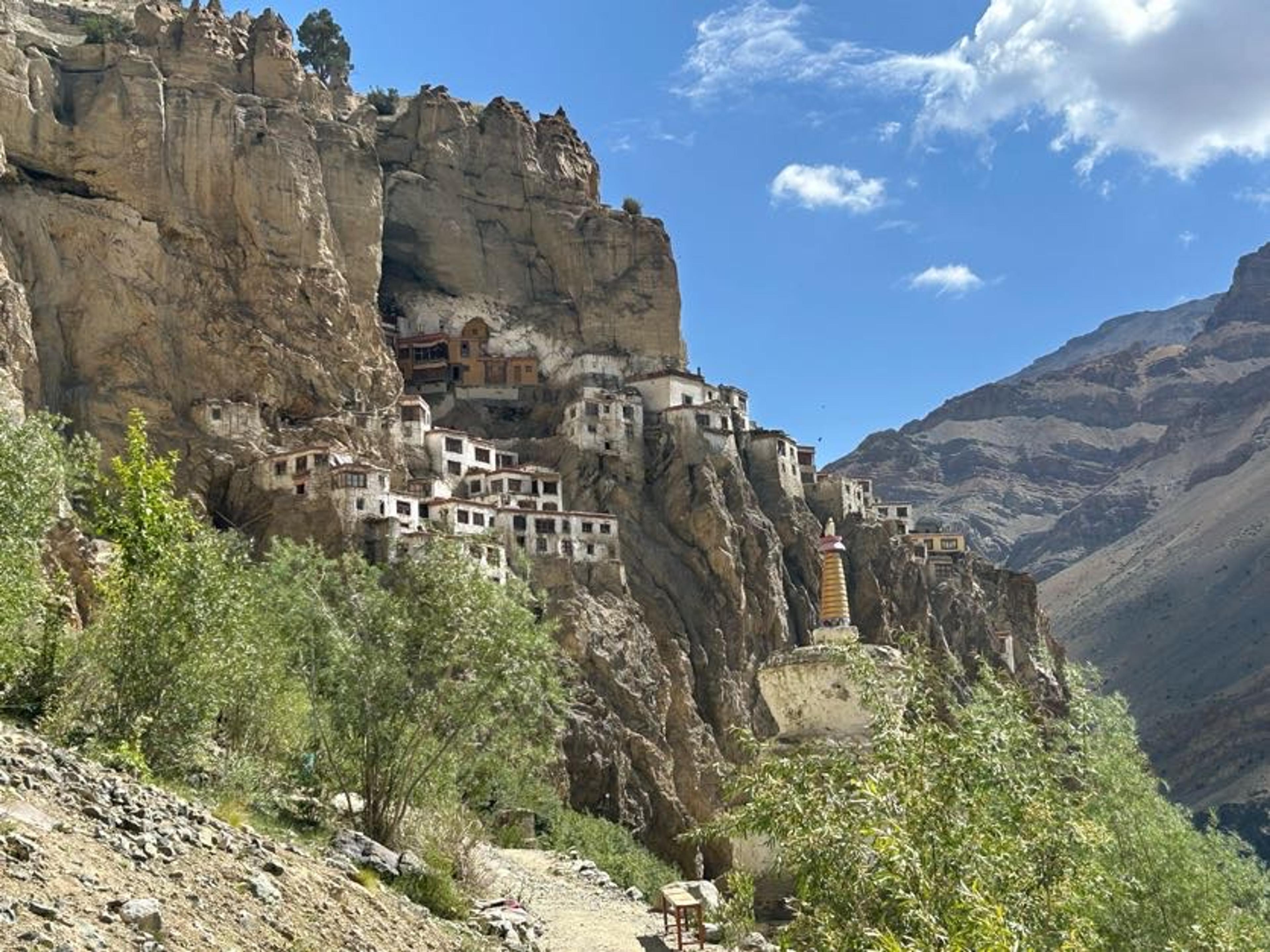 Phugtal monastery's buildings clinging to a cliff around a large cave mouth, with a gold-topped chorten on the trail below