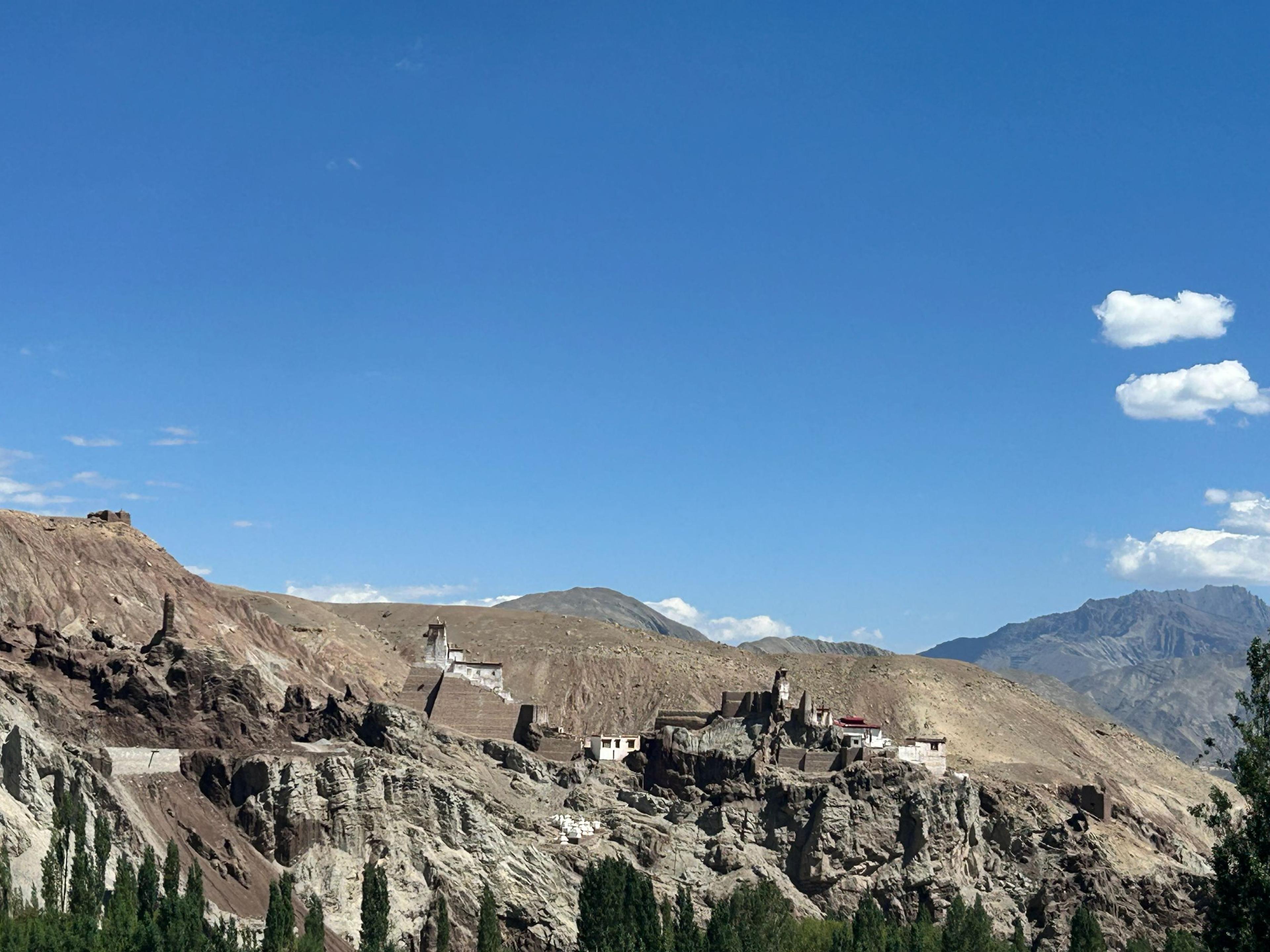 Ruined fort and temples of Basgo on eroded clay cliffs above poplar trees, under a deep blue sky