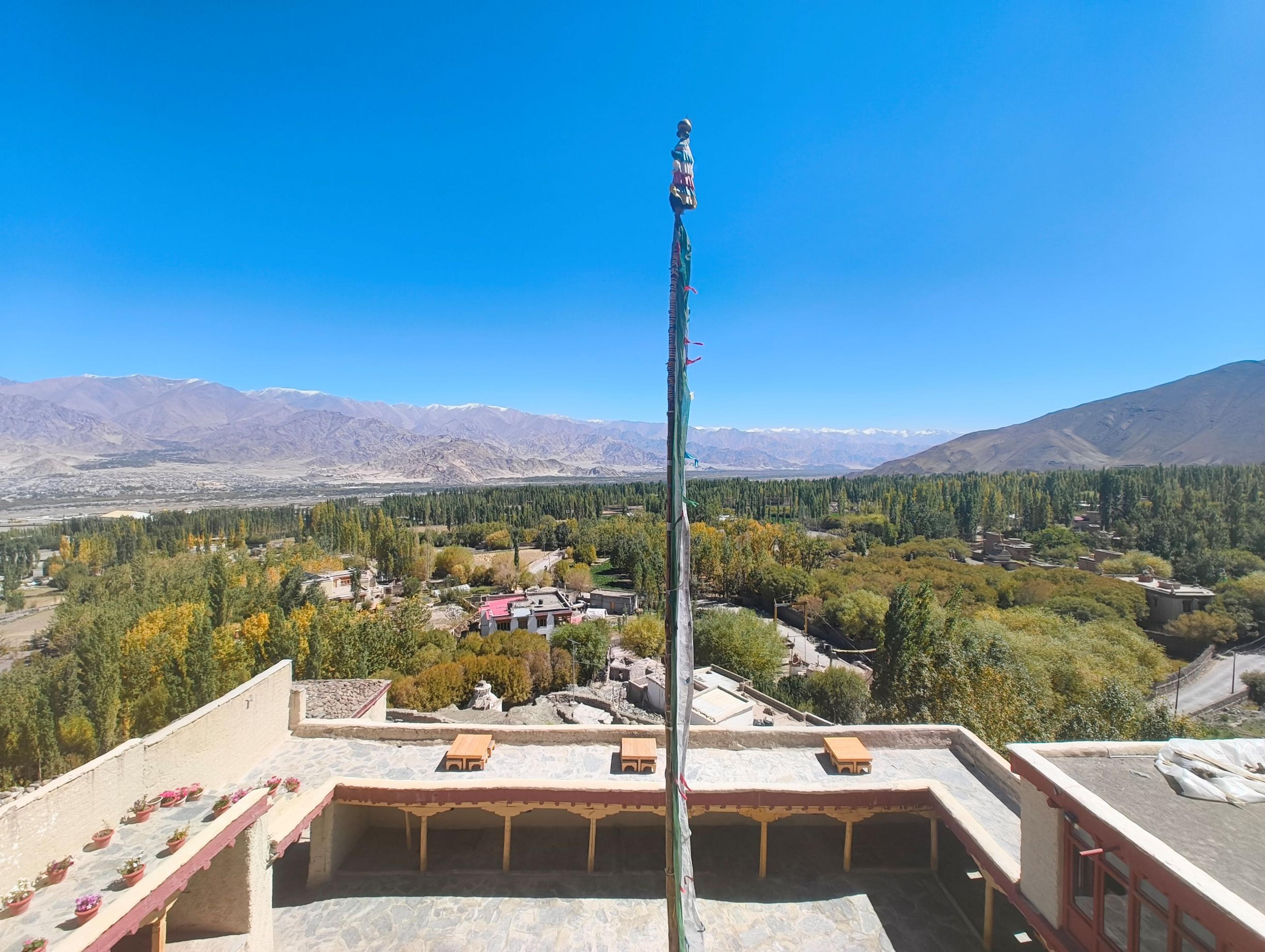 Rooftop terrace with a prayer flag pole, overlooking Stok village's autumn poplars and the Indus valley, mountains beyond