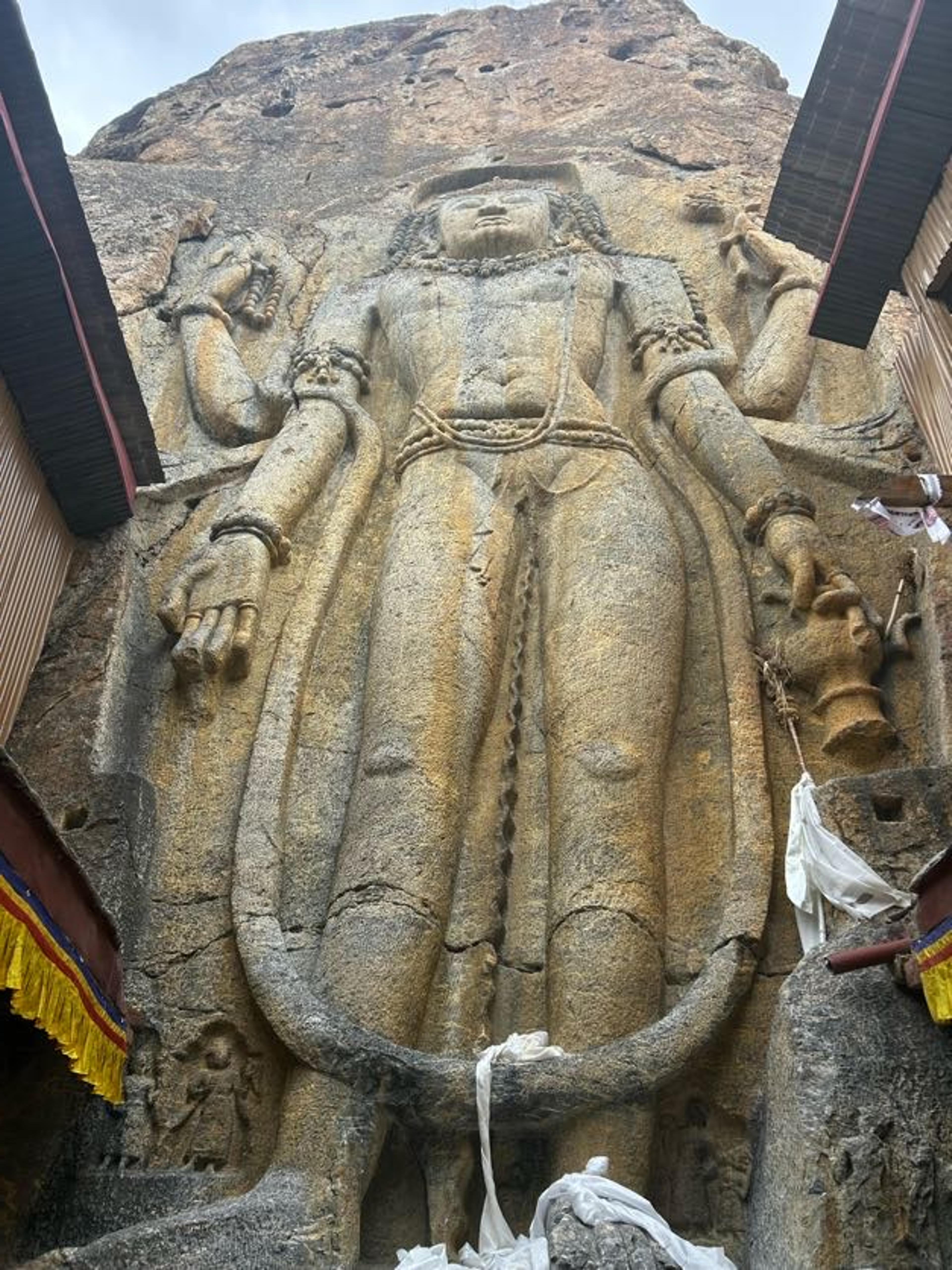 Tall standing four-armed Maitreya Buddha carved in relief into a rock face at Mulbekh, with white khatags at its feet