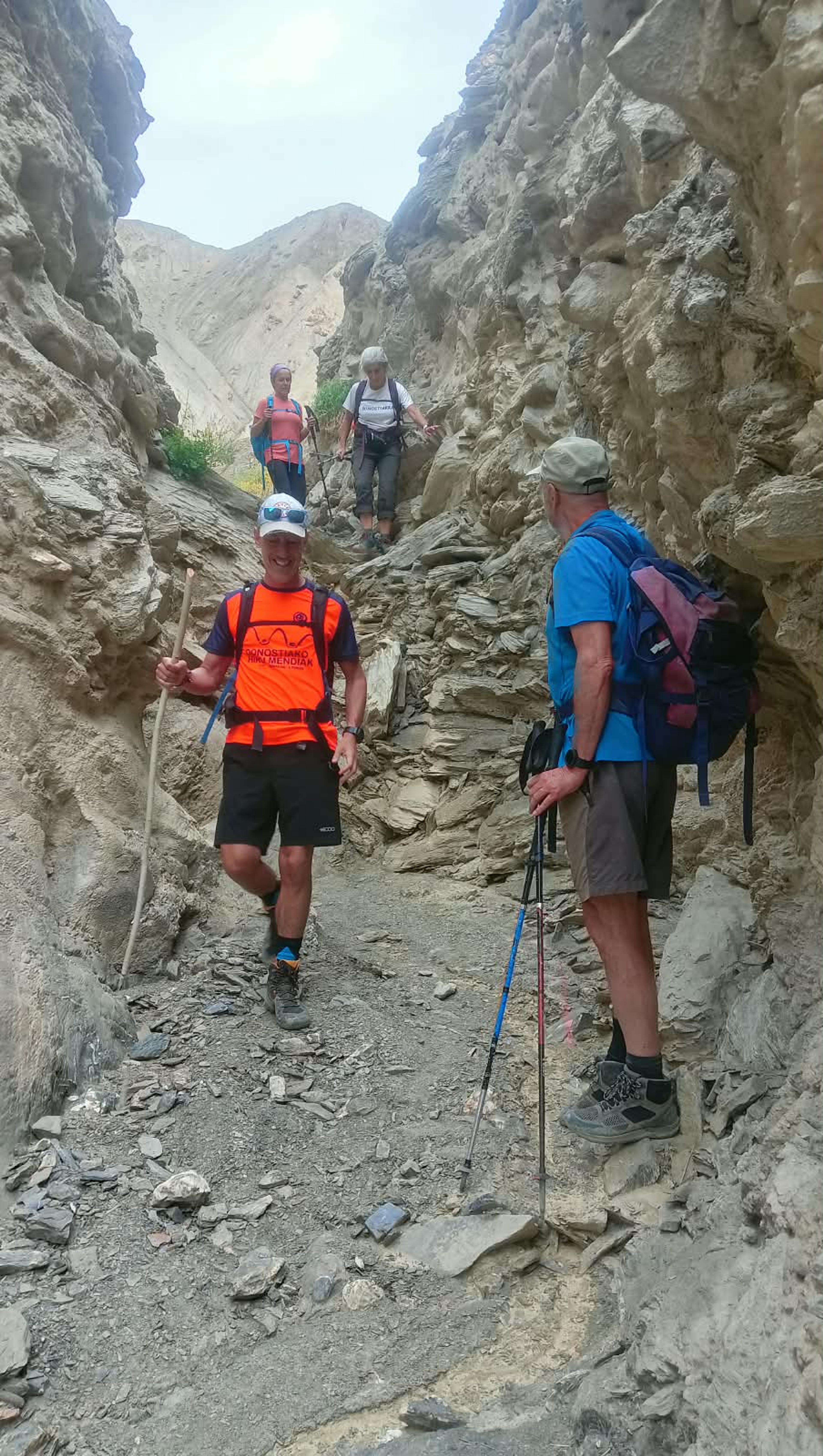 Smiling trekkers with poles scrambling down a narrow gully of pale, eroded rock walls