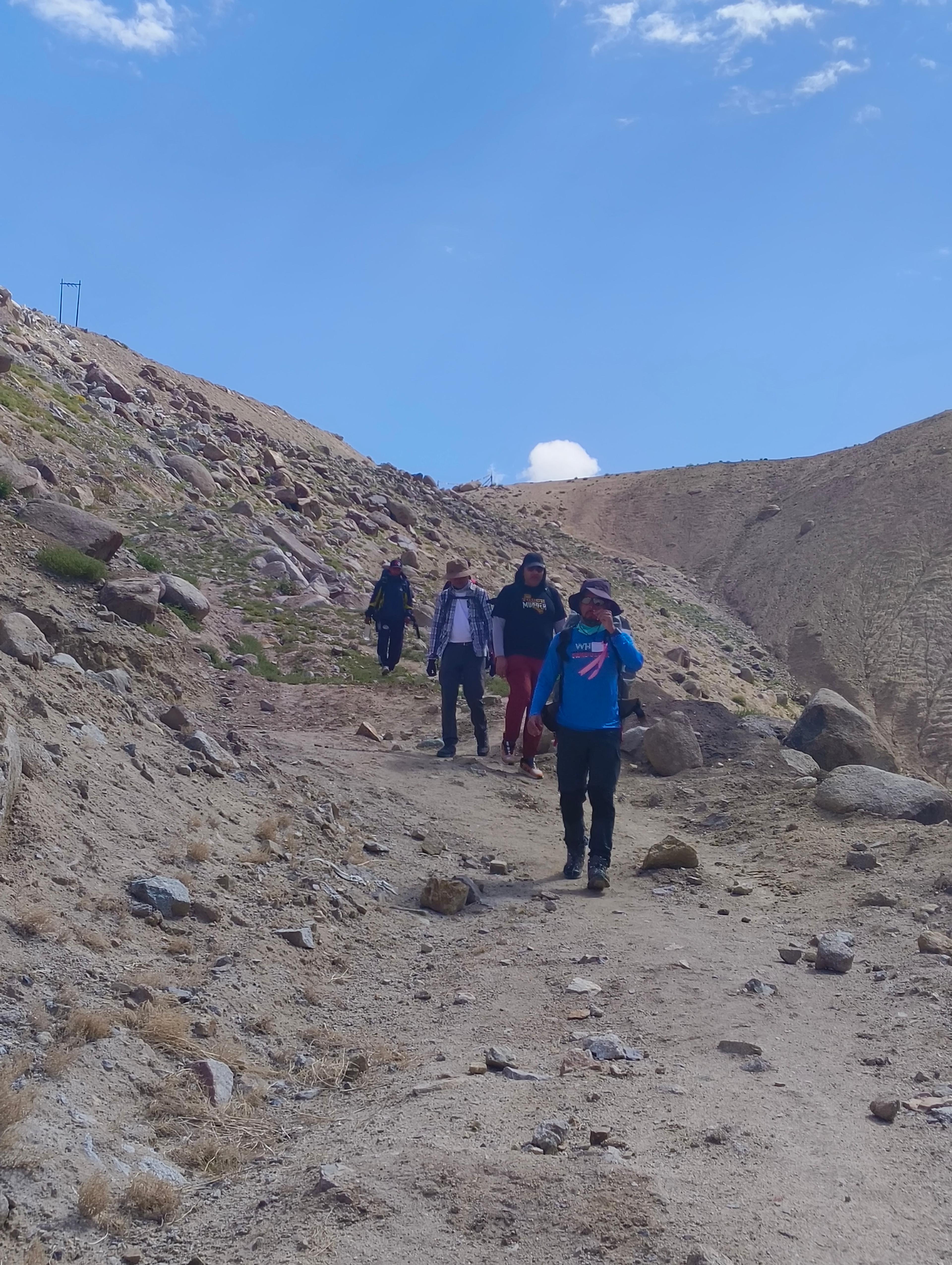 Small group of trekkers walking down a dusty, rocky trail under a clear blue sky