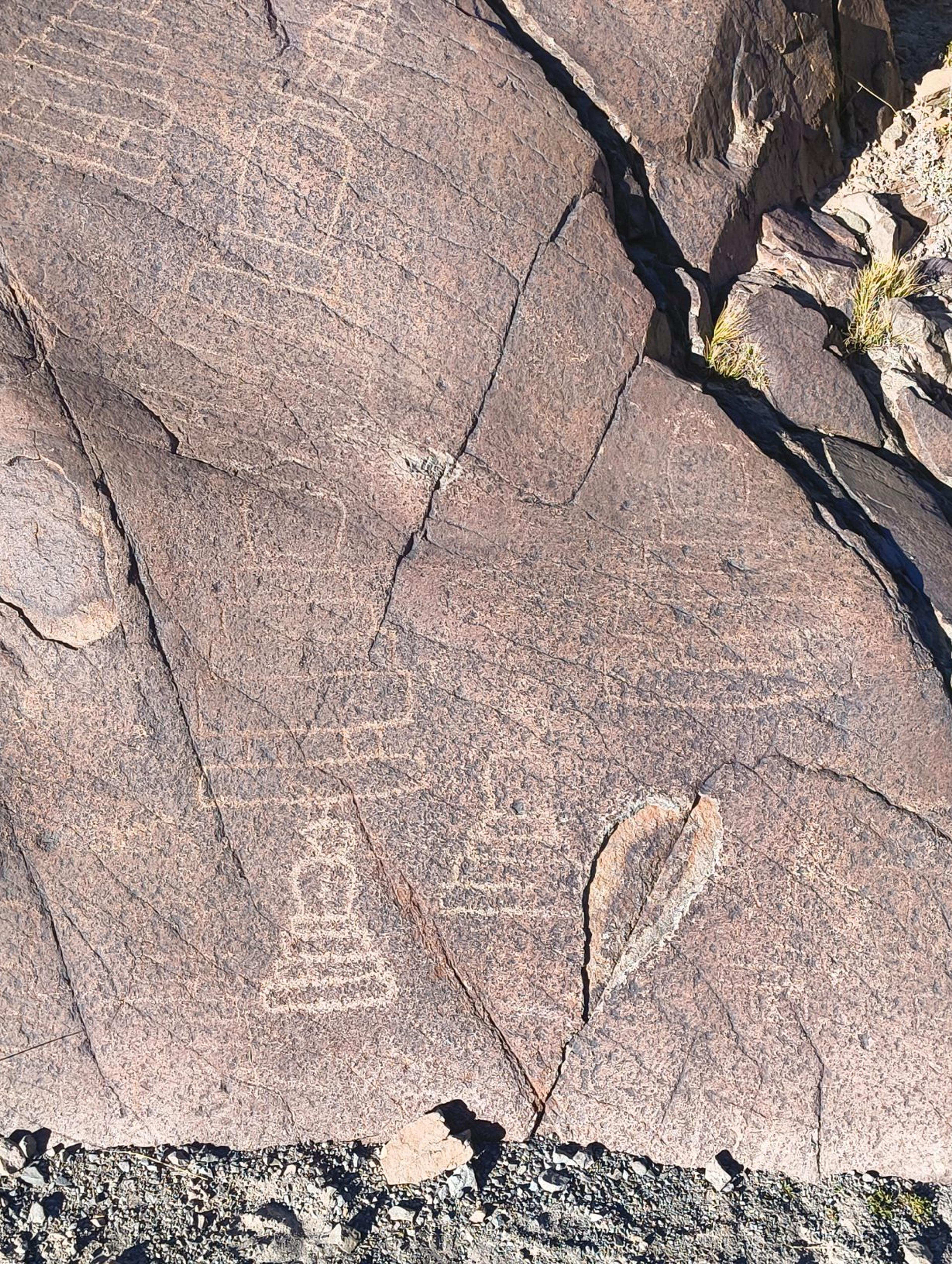 Outlines of Buddhist chortens carved into a dark, weathered rock face beside a stony trail