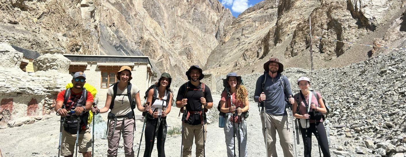 A Voyager Ladakh trekking group with poles and backpacks beside a village chorten in a rocky Ladakh gorge