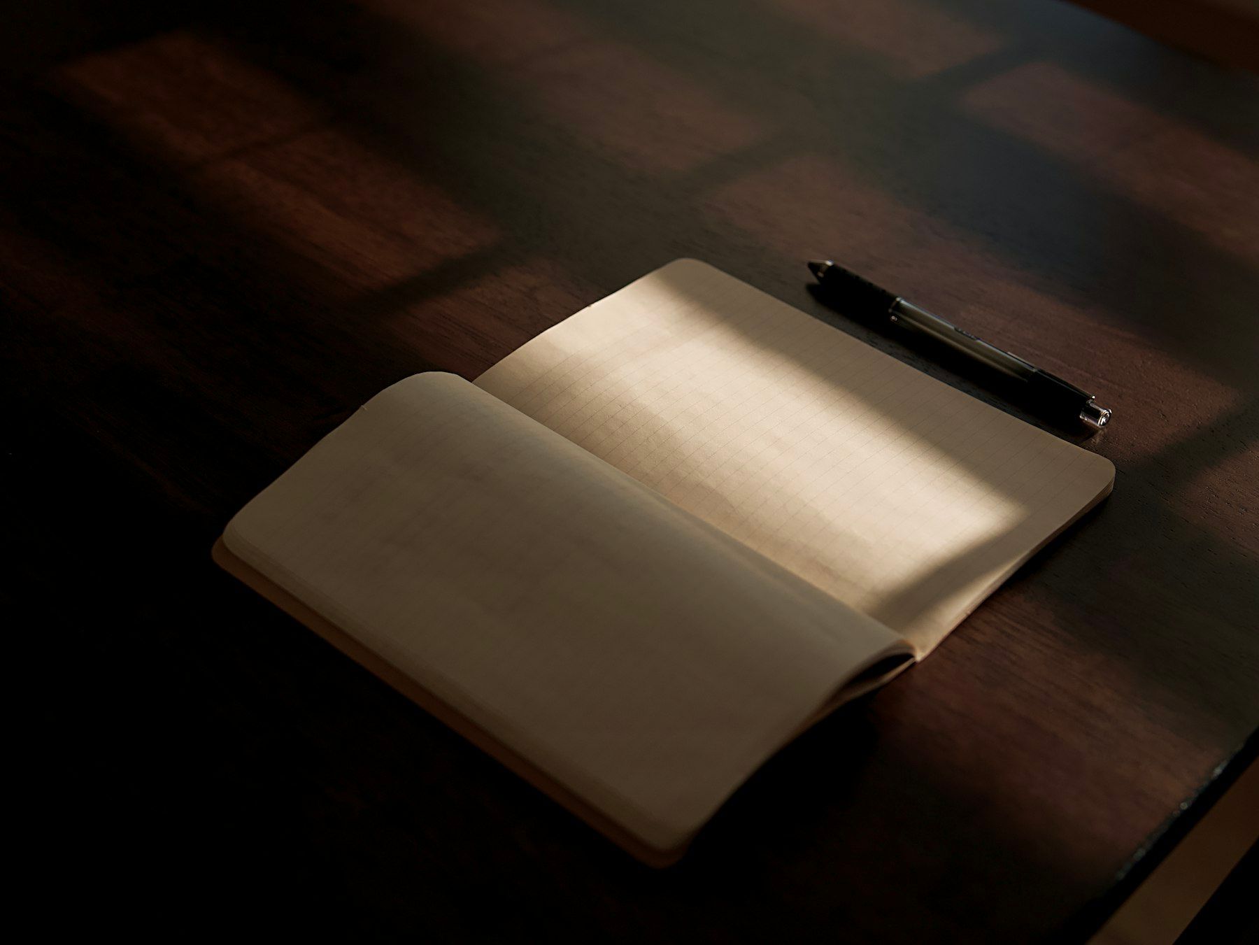 Open cream notebook with a black pen resting on a wooden desk in soft natural light.