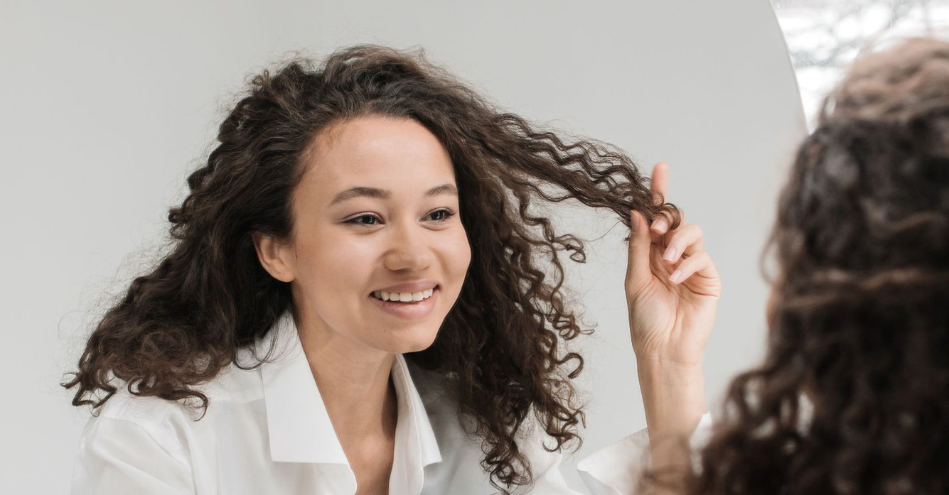 vrouw met krullend haar voor spiegel