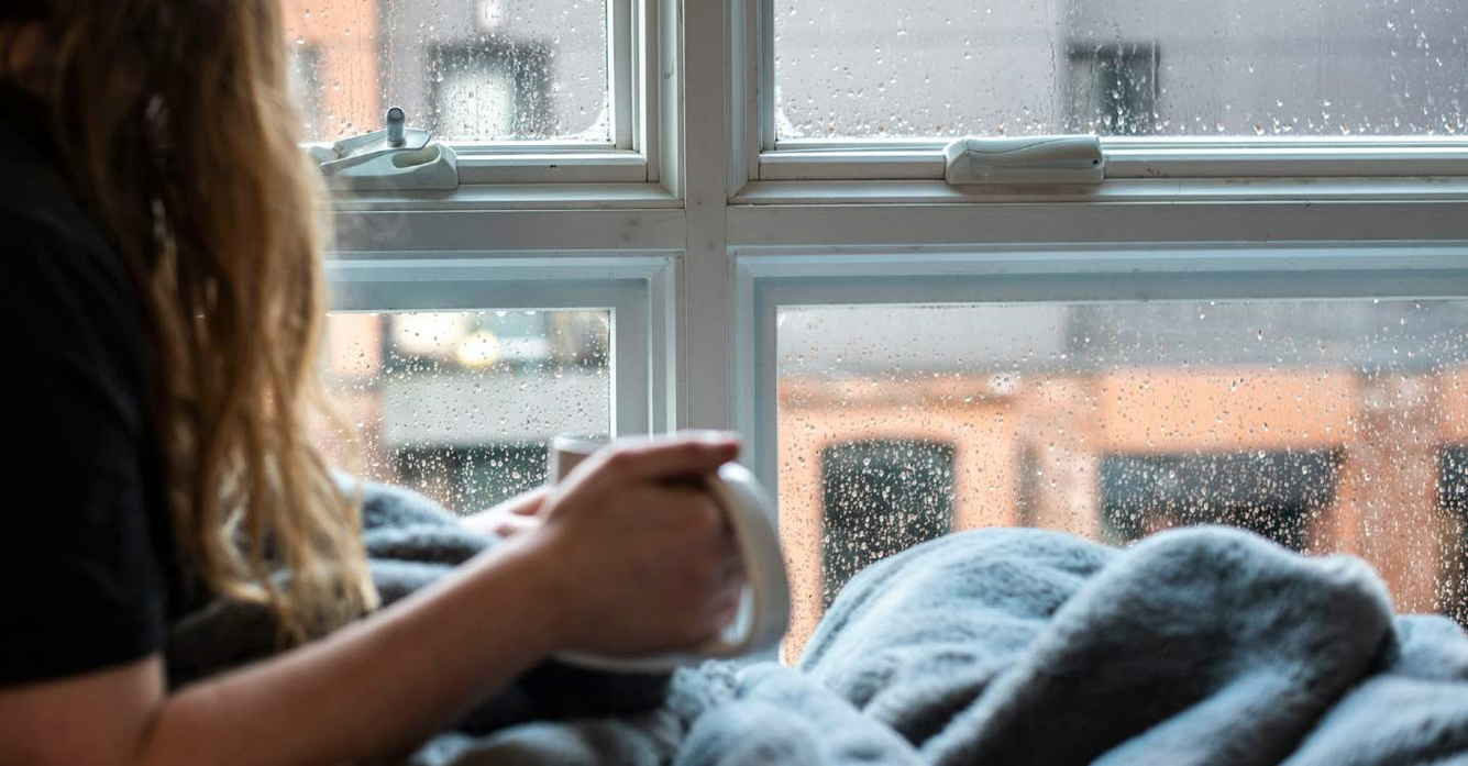 Vrouw die door het raam naar buiten kijkt terwijl het buiten regent.