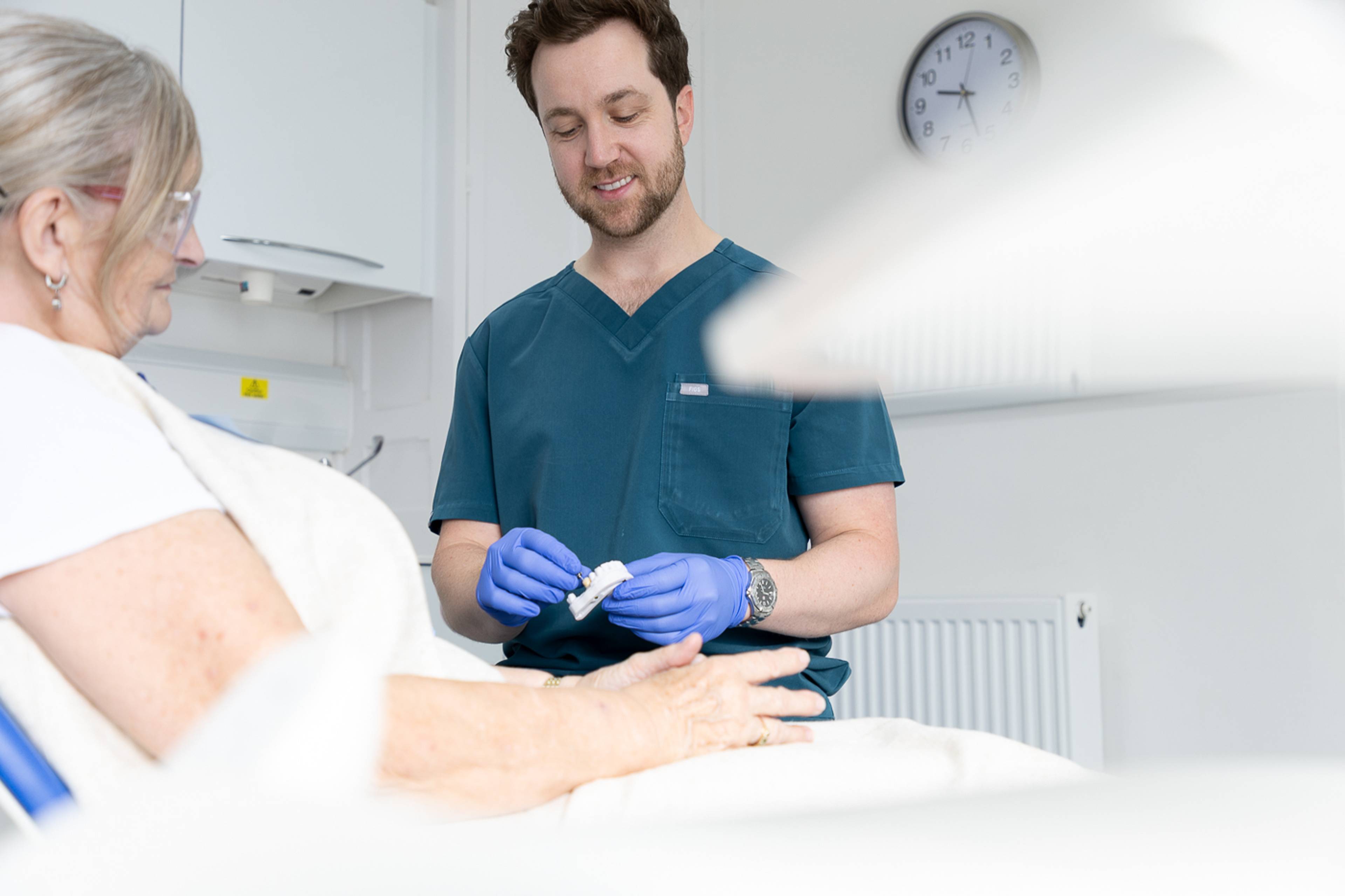Tom Mann speaking to a patient with a model of a lower jaw in his hand