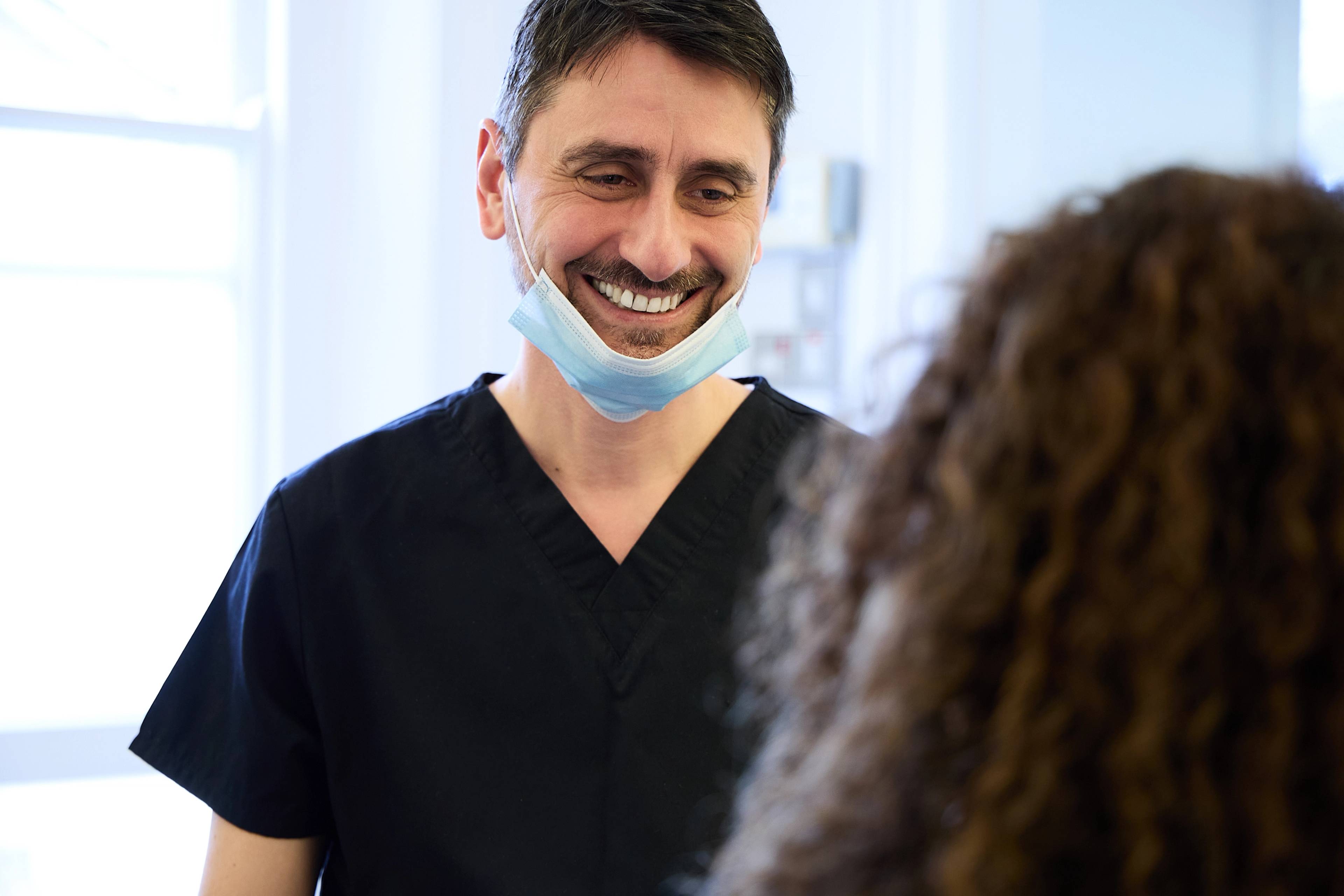 Oreste Gheorghe smiling while talking to a patient with a face mask pulled down around his chin
