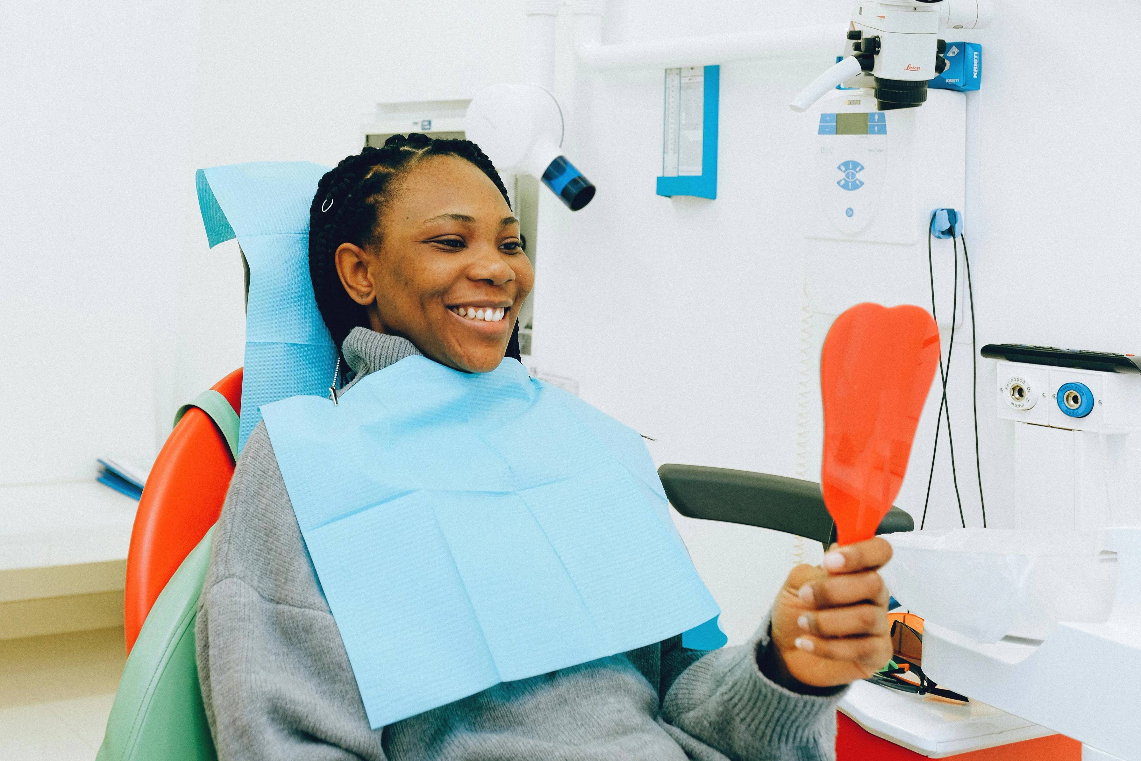 A stock photo of a woman looking in a hand mirror while in a dentists chair