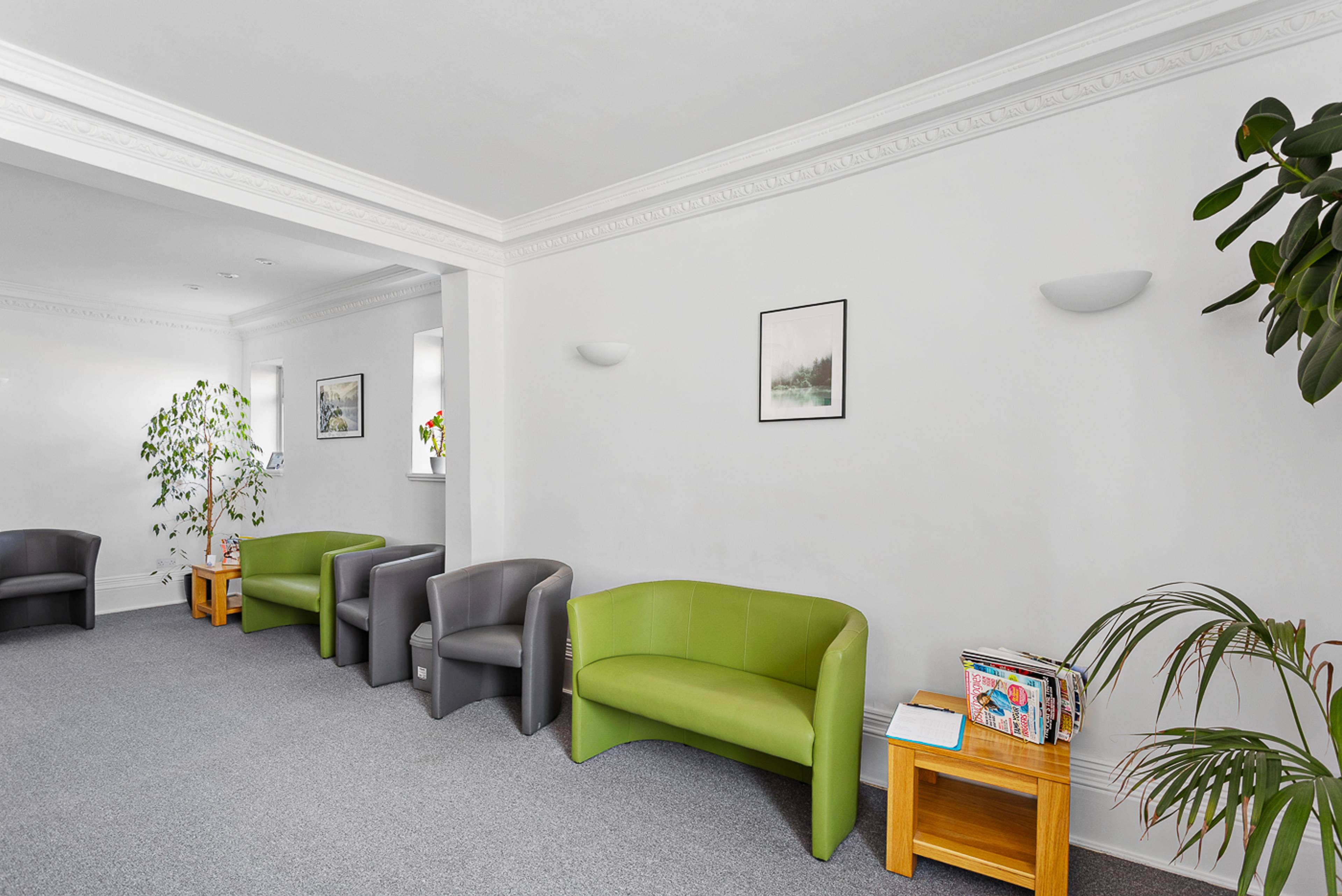 Our reception area, with green and grey sofas, grey carpet, white walls, and many plans