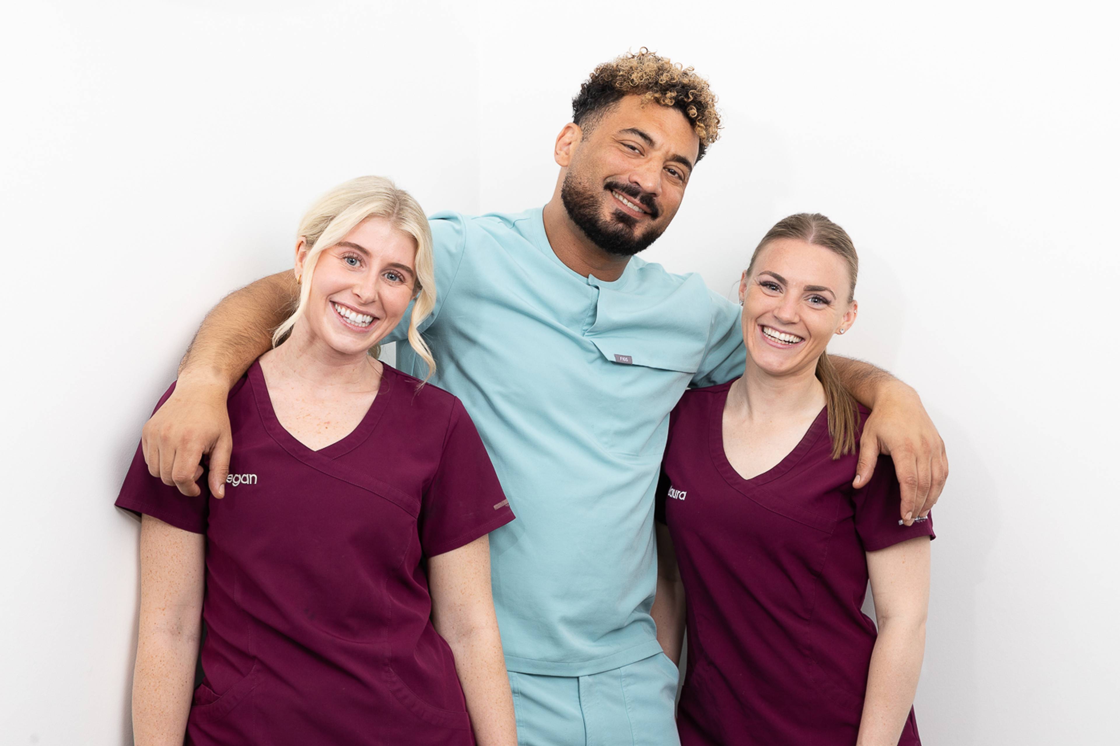 A dentist and two dental nurses smiling