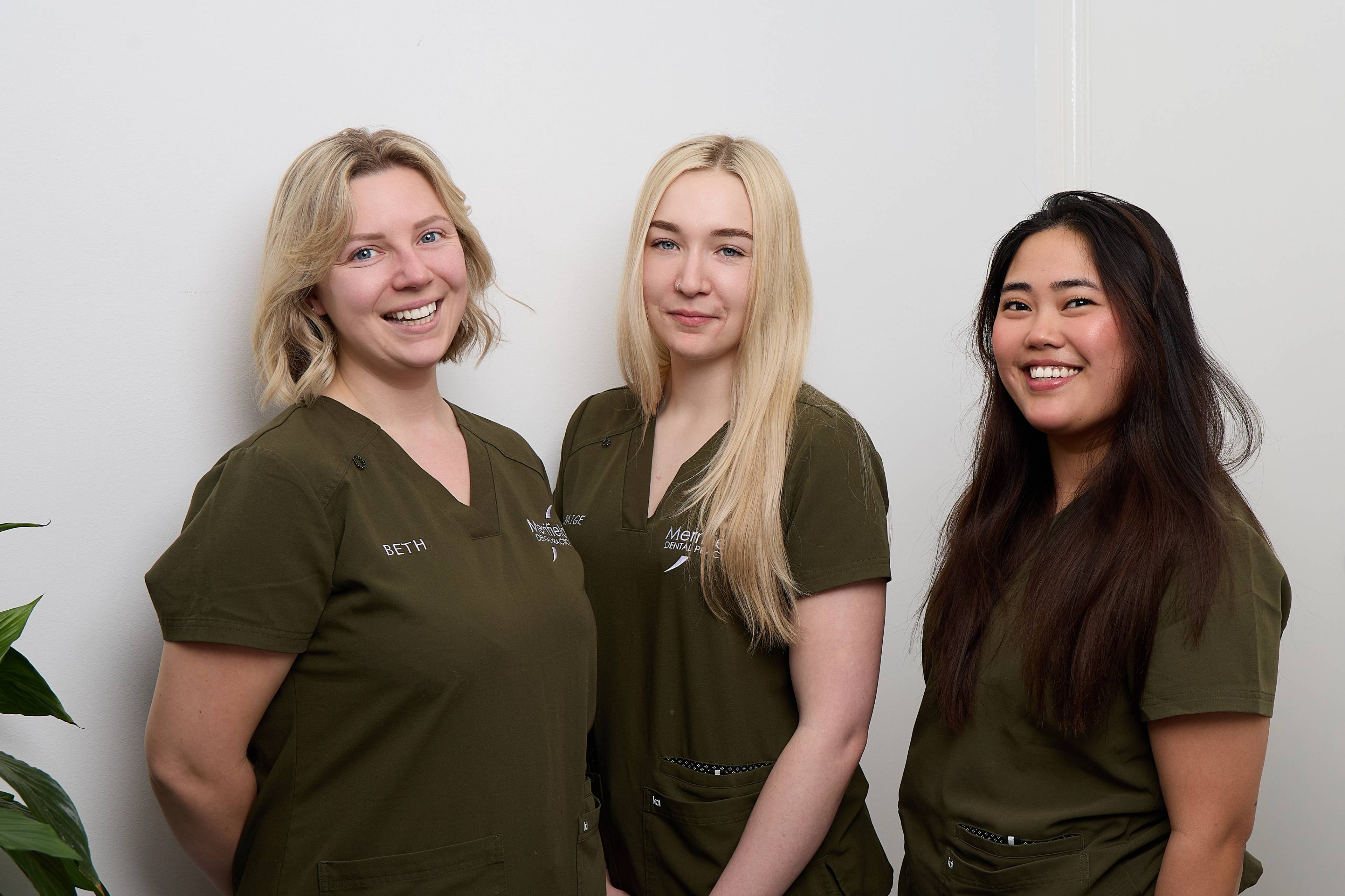 Merrifield Dental team 3 nurses in matching dark green scrubs smiling together for a photo
