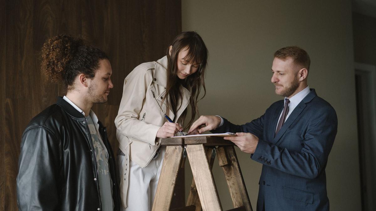Three individuals signing a contract on a ladder inside a new house, symbolizing a real estate deal.