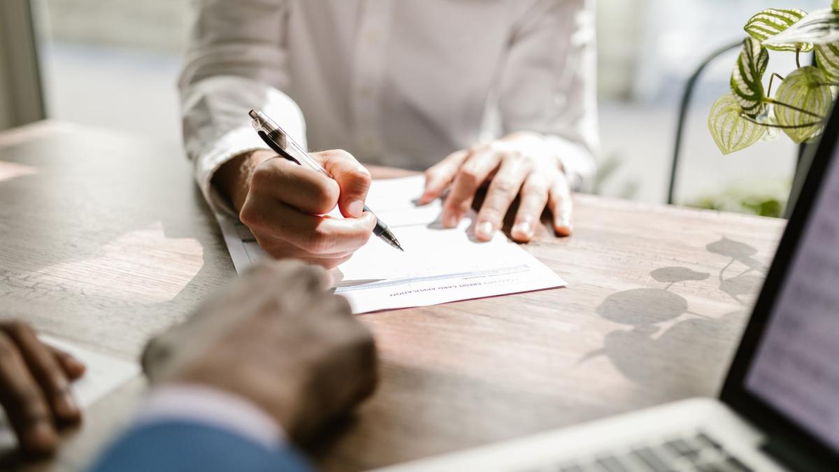 Close-up of people signing a document at a desk, highlighting professional business interaction.