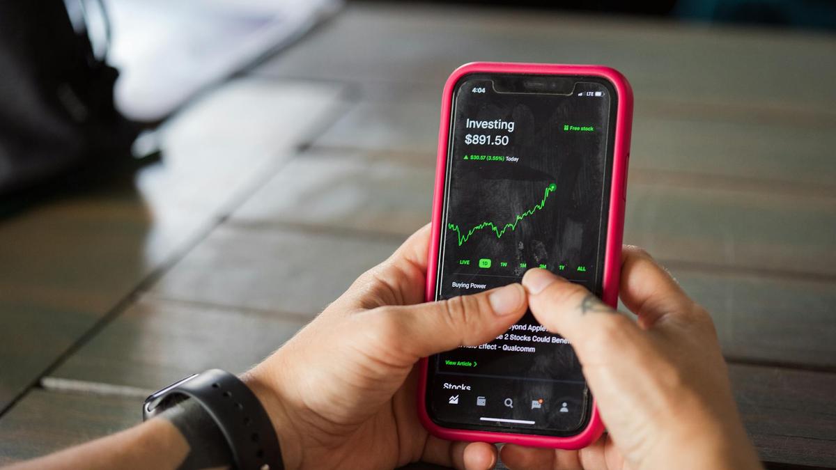 A person holding a smartphone with a stock market app displaying analytics and stock prices.