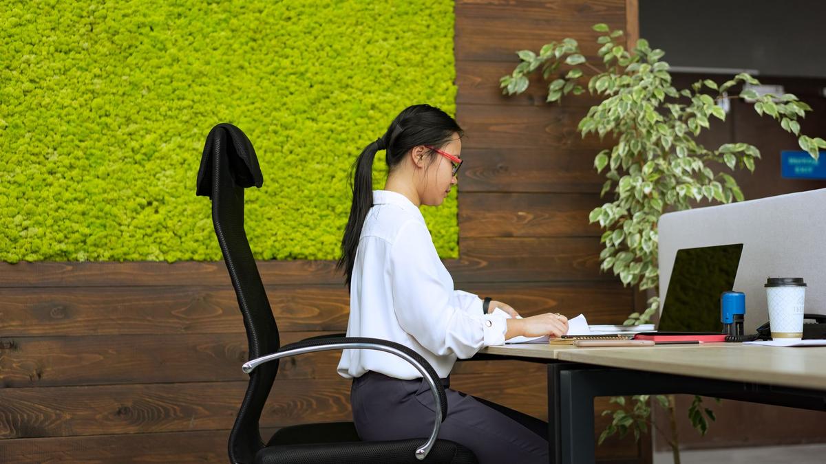 Woman working at her desk in a modern office with green moss wall and plants.