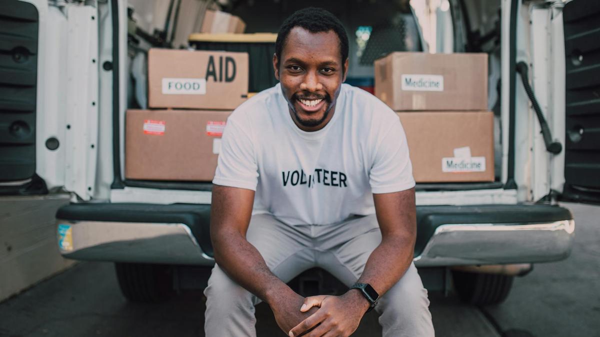 Smiling volunteer seated with boxes labeled food and medicine in a van.