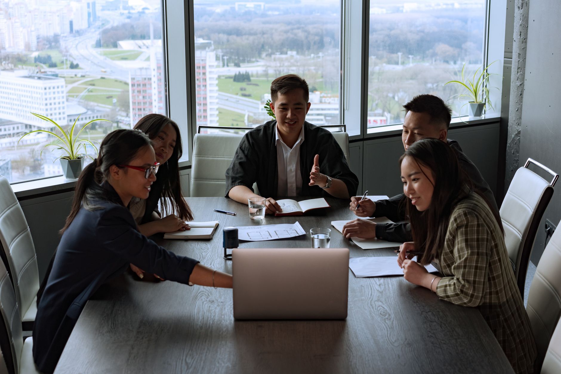 A diverse group of professionals engaged in a meeting in a modern office setting overlooking the city.
