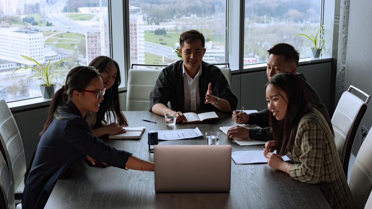 A diverse group of professionals engaged in a meeting in a modern office setting overlooking the city.