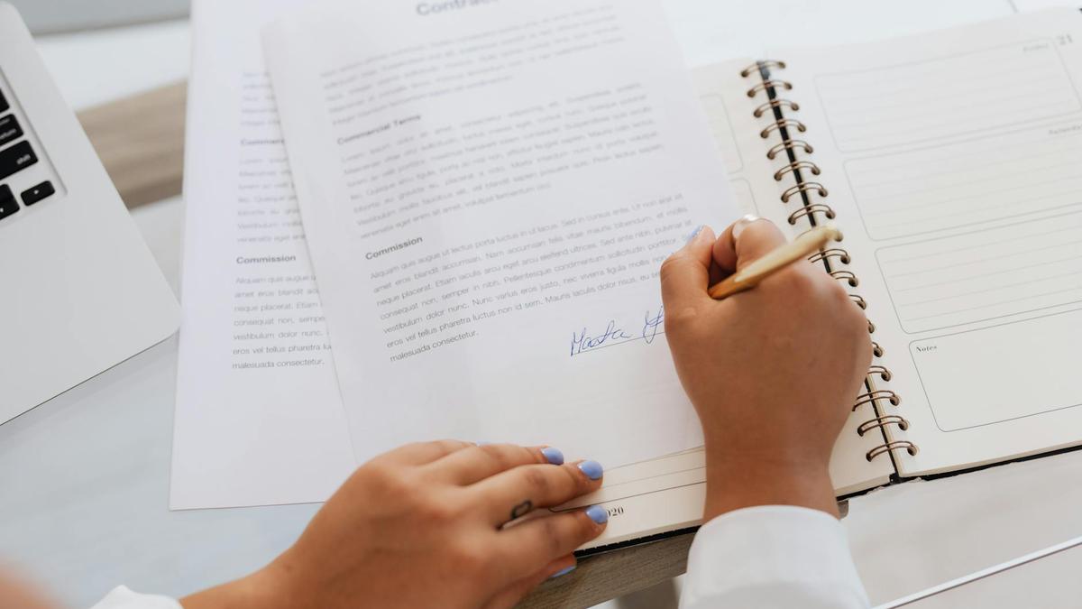Close-up of hands signing a contract on a desk with office supplies, symbolizing legal agreements.