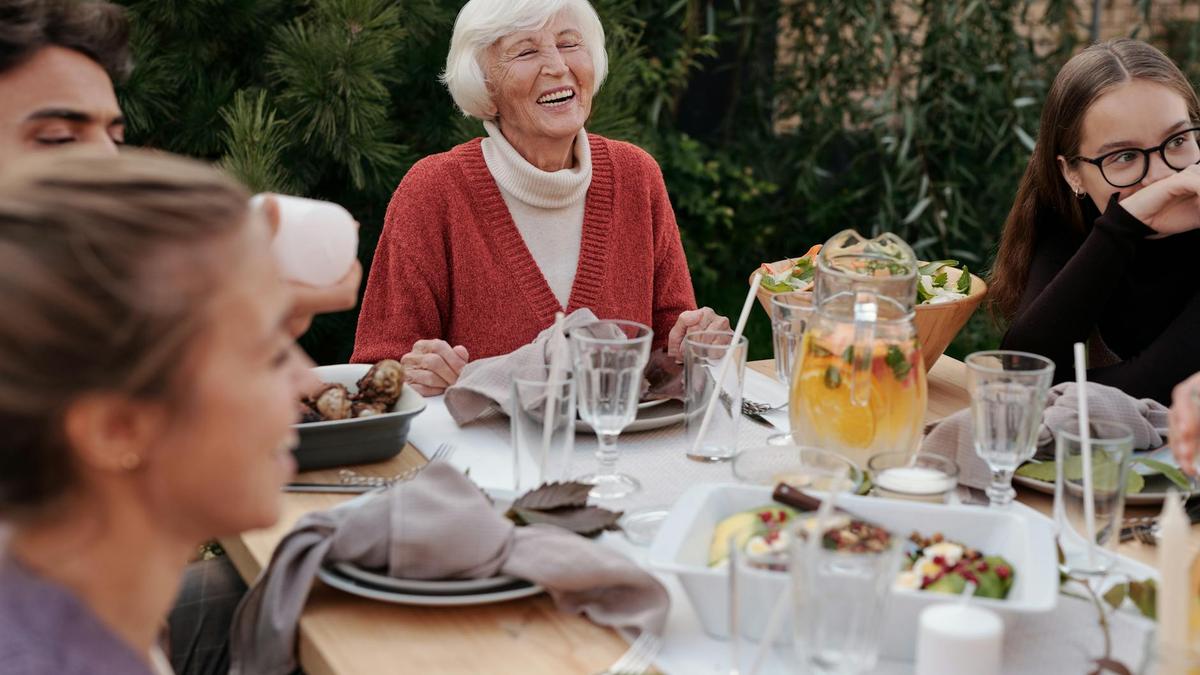 Smiling elderly woman with family and friends enjoying dinner at table backyard garden