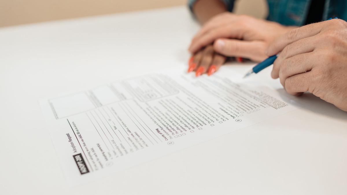 Close-up of hands signing adoption papers in an office environment, symbolizing family and legal process.