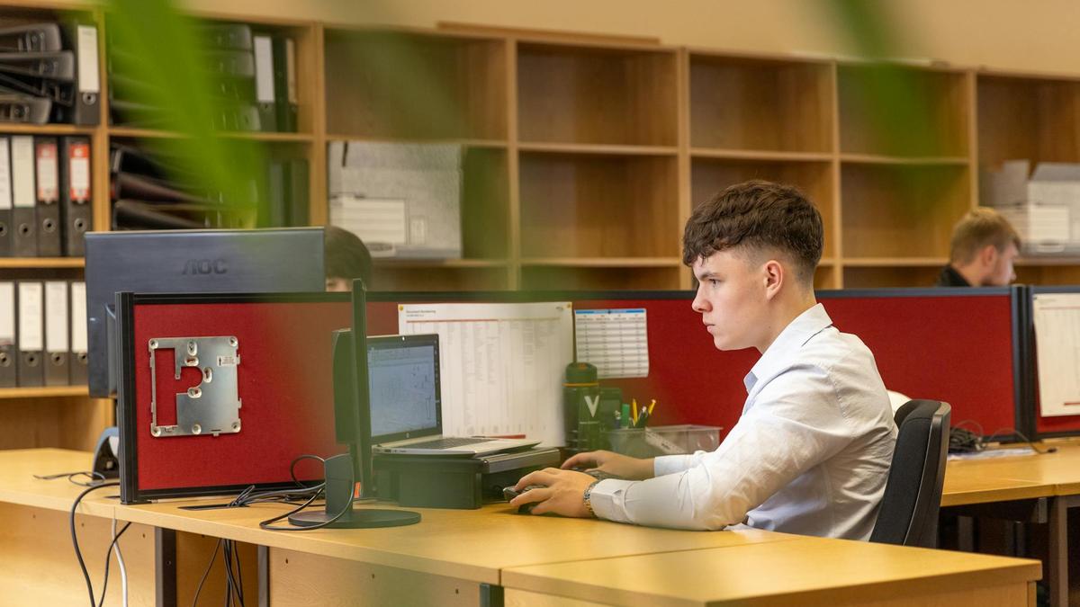 A focused young man typing on a computer in a contemporary office environment.