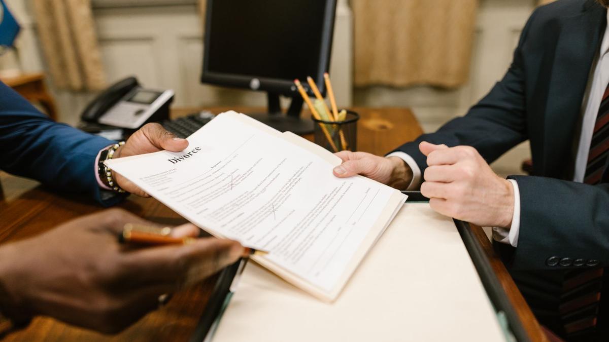 Close-up of hands exchanging divorce documents during legal proceedings in office.