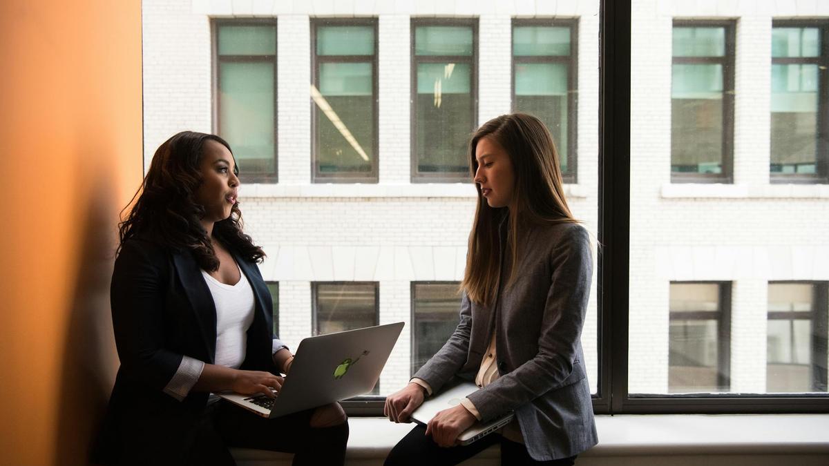 Two women having a business discussion in an office setting, using a laptop.
