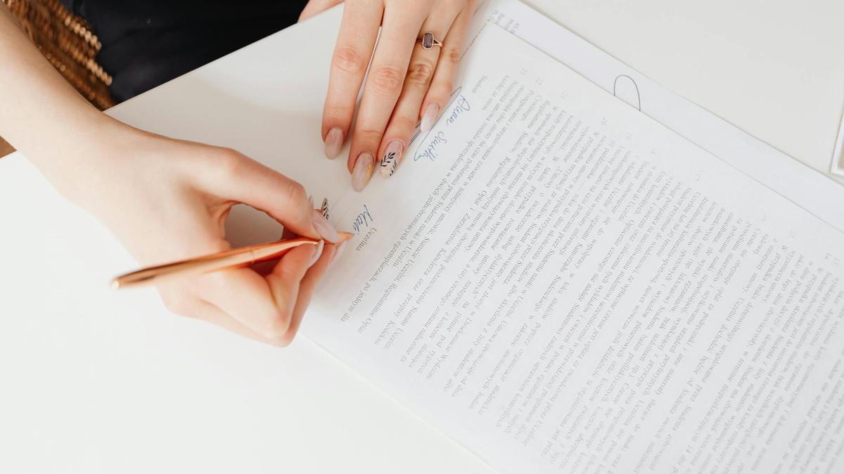 Close-up of woman's hands signing a legal document with elegant nail art using a pen.