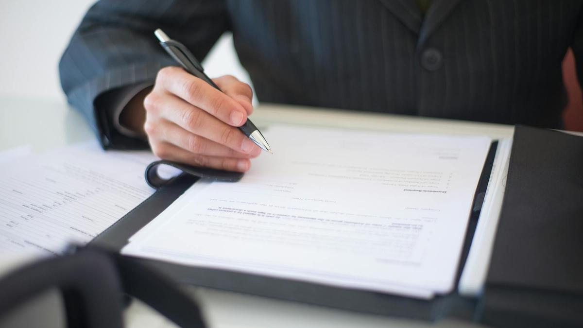 Close-up of a hand signing documents with a pen, symbolizing an important business contract.