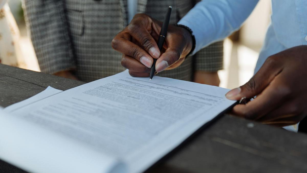 Close-up of business professionals signing a document with a pen indoors.