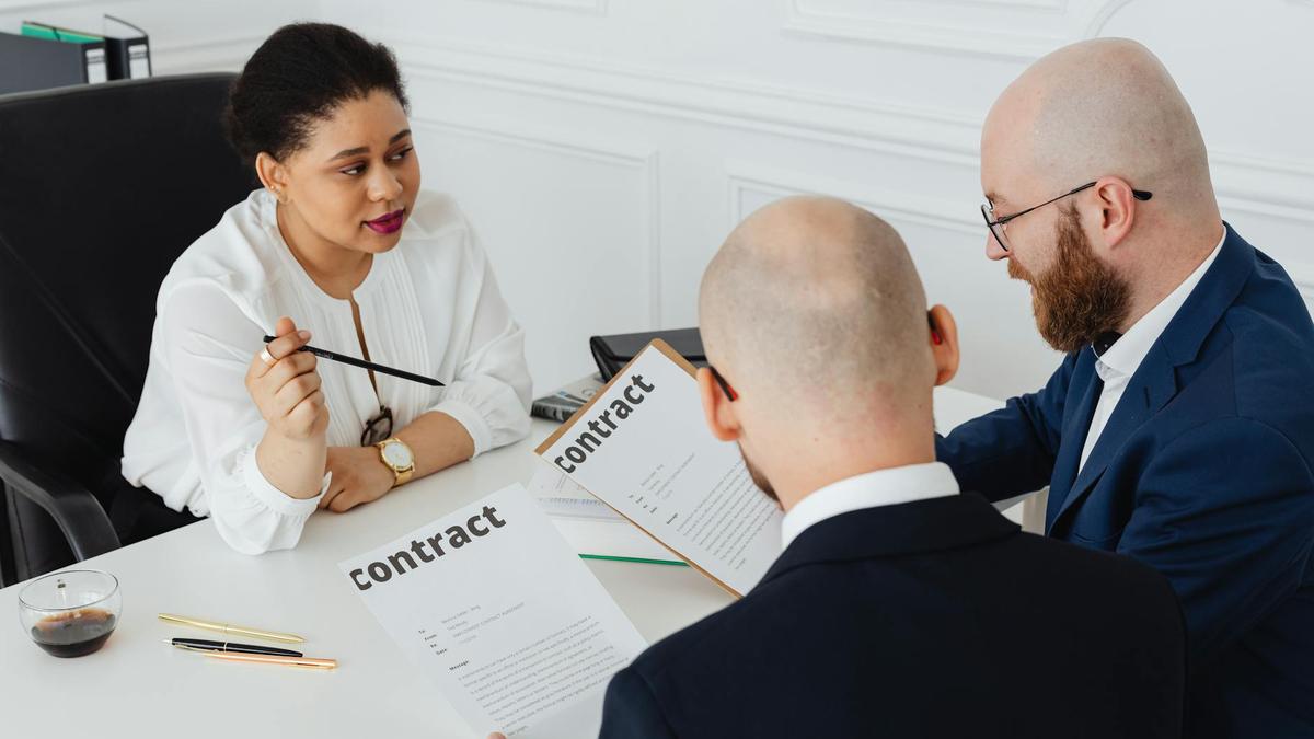 Three business professionals in discussion over a contract in a modern office setting.