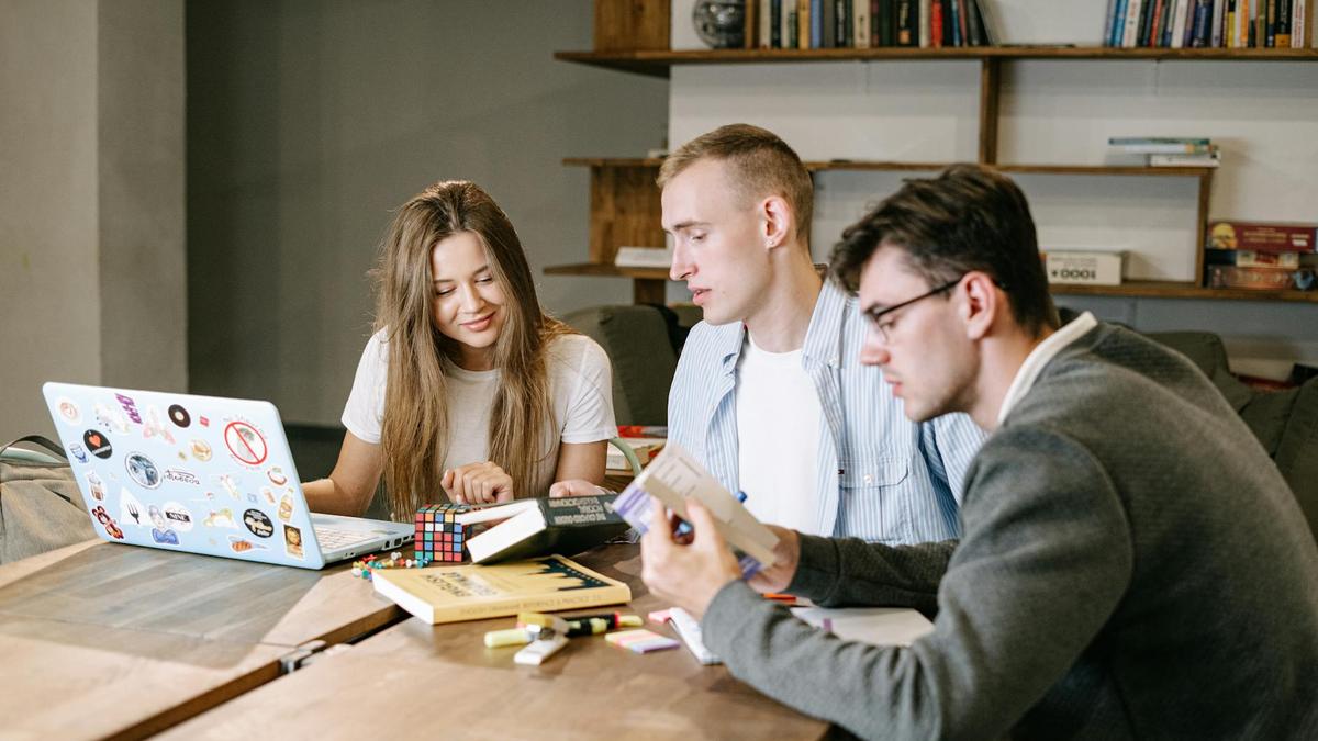 A group of young professionals collaborating on a project in a modern office space, working with books and a laptop.